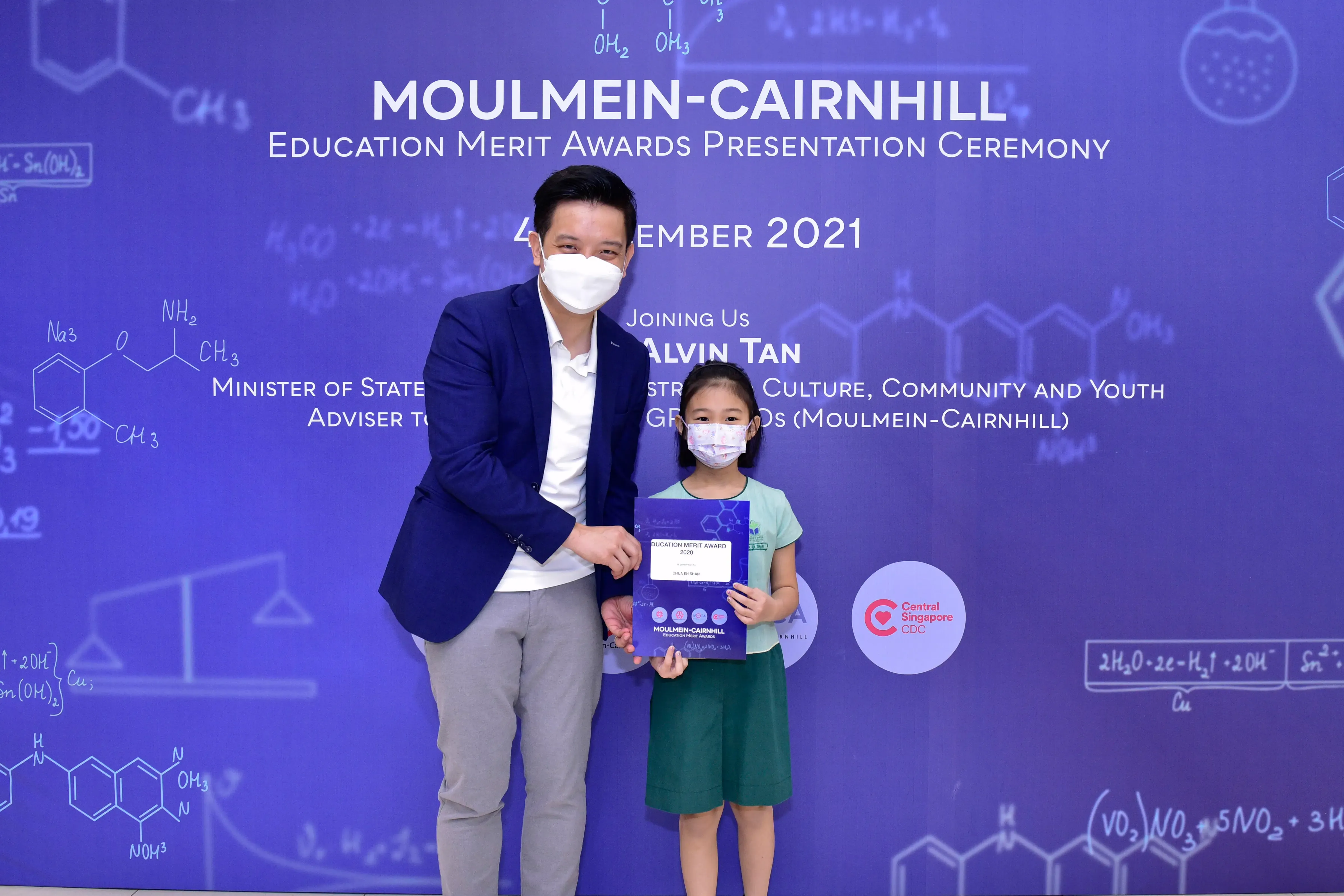 A masked man and young girl hold an award certificate at the Moulmein-Cairnhill Education Merit Awards 2021.
