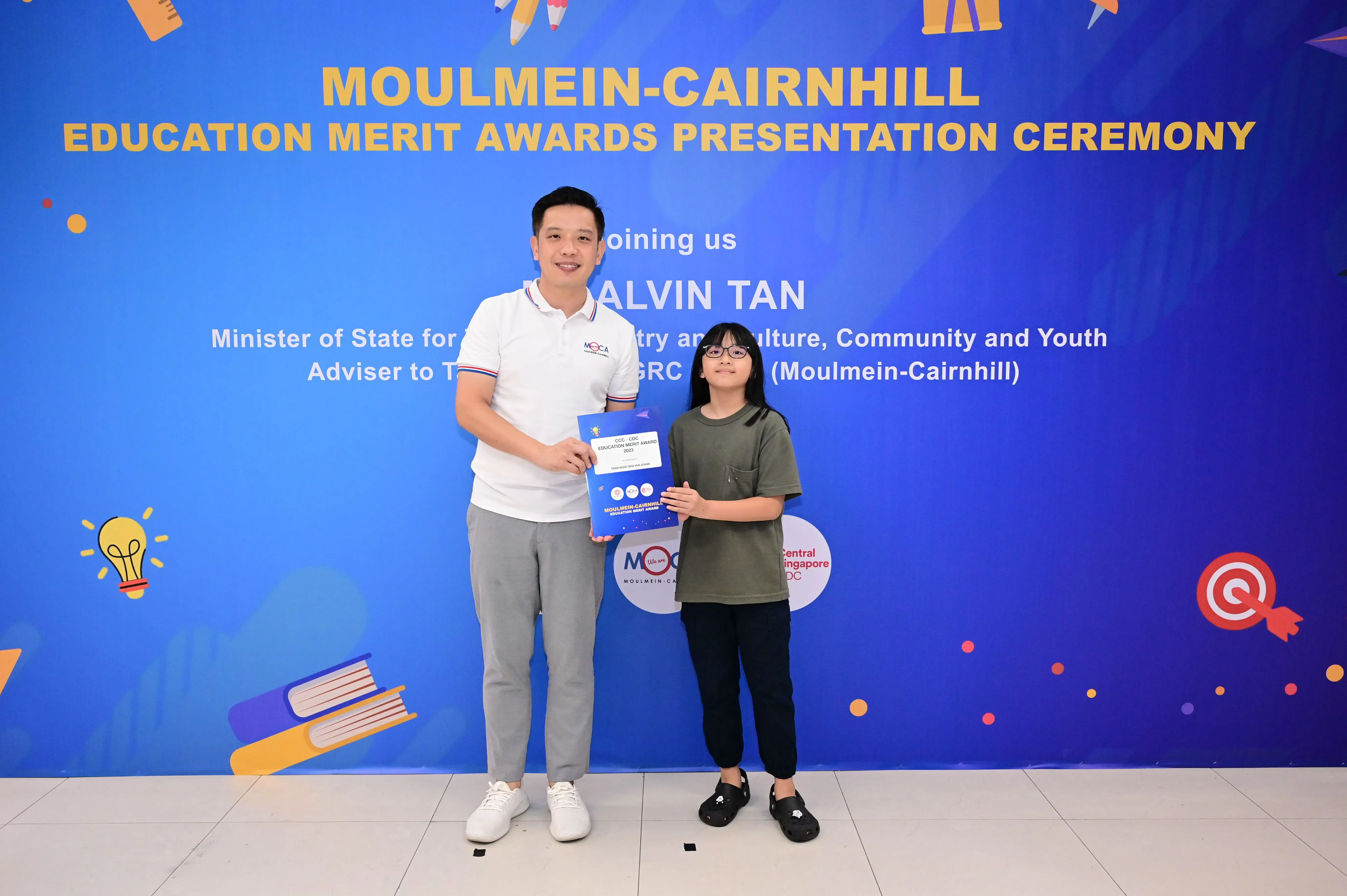 A man and a young girl hold an award certificate at the Moulmein-Cairnhill Education Merit Awards Presentation Ceremony.