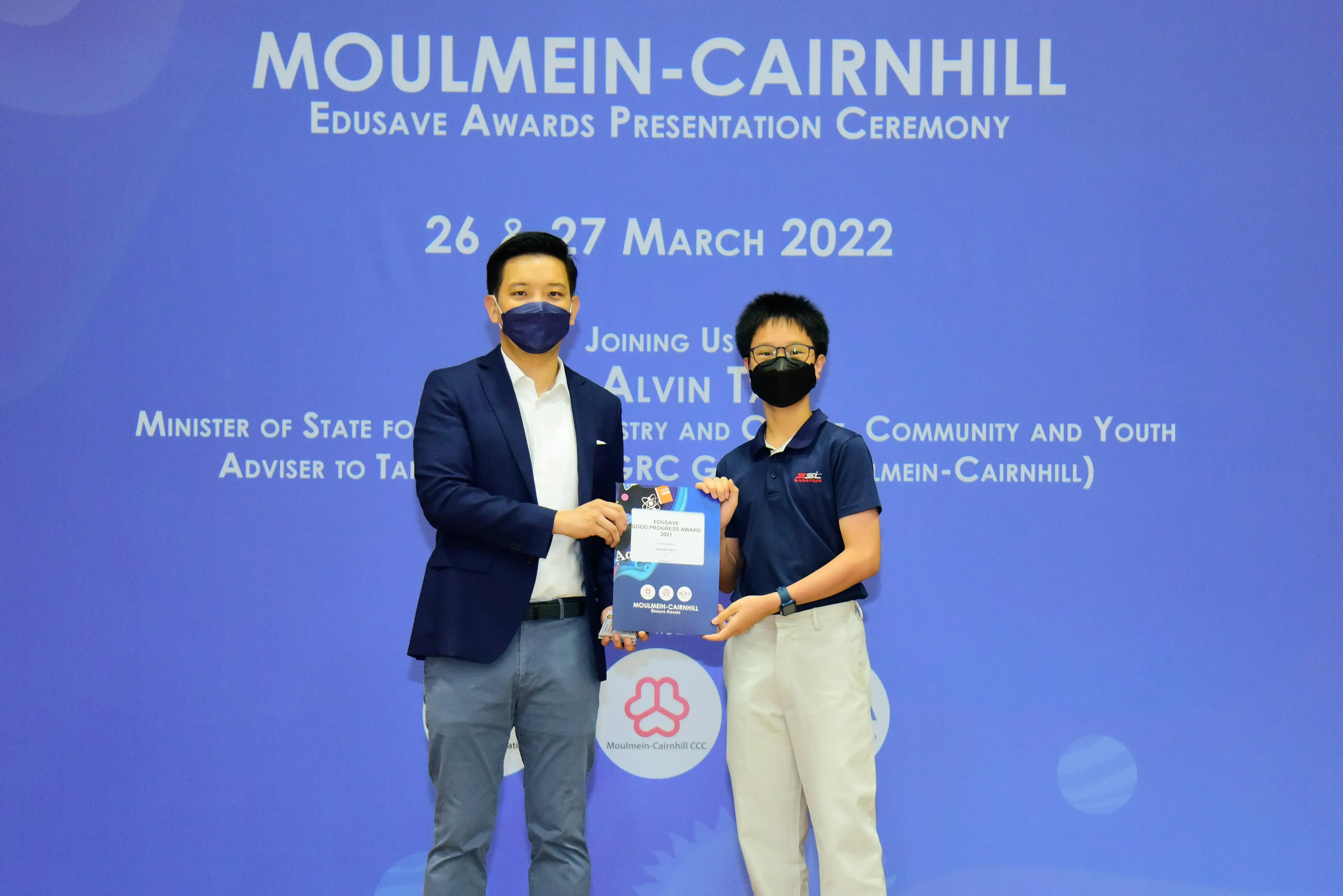 Two masked men hold an award certificate at the Moulmein-Cairnhill Edusave Awards Presentation Ceremony, March 2022.