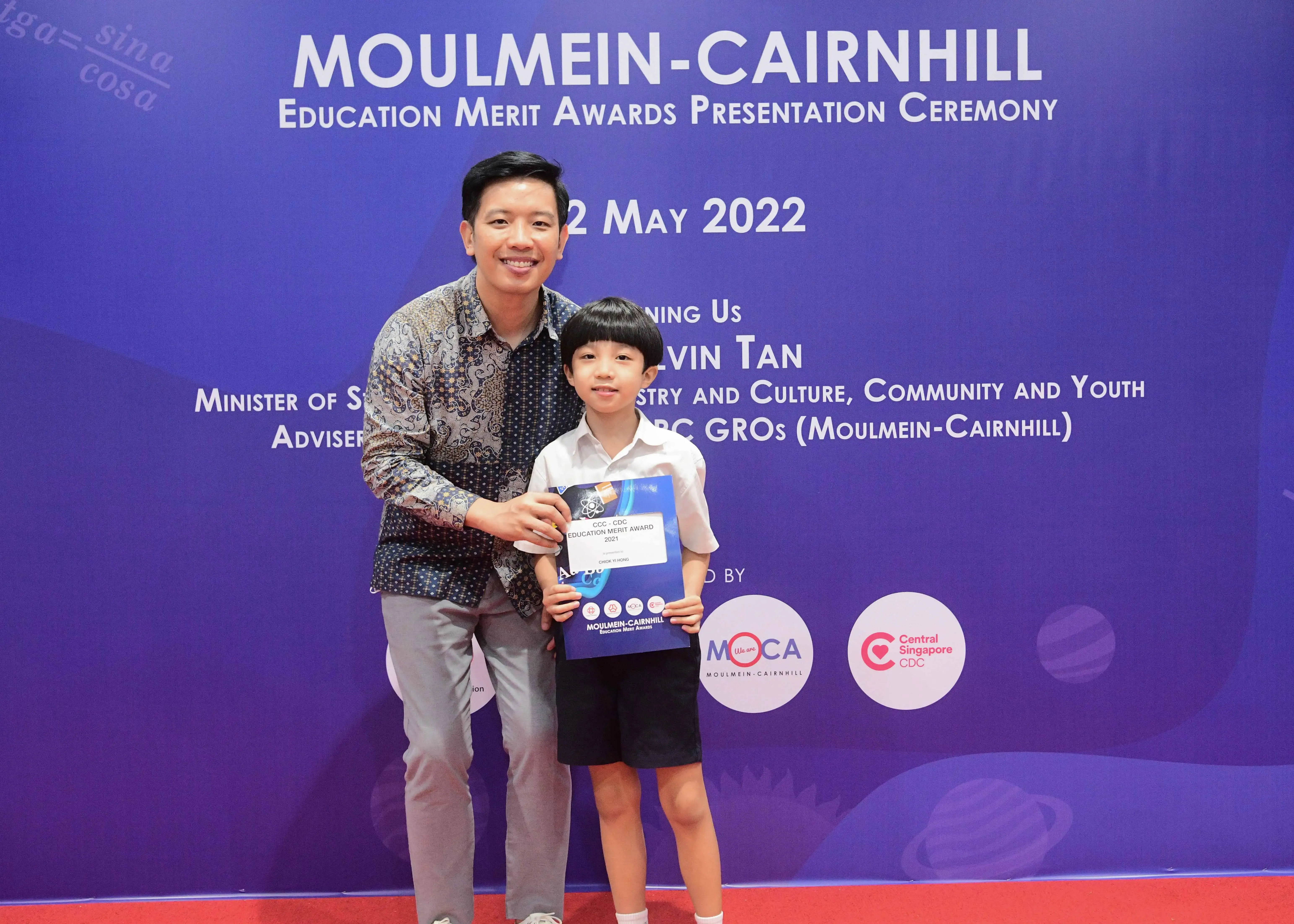 A man and a young boy holding an award certificate at the Moulmein-Cairnhill Education Merit Awards Ceremony, May 2022.