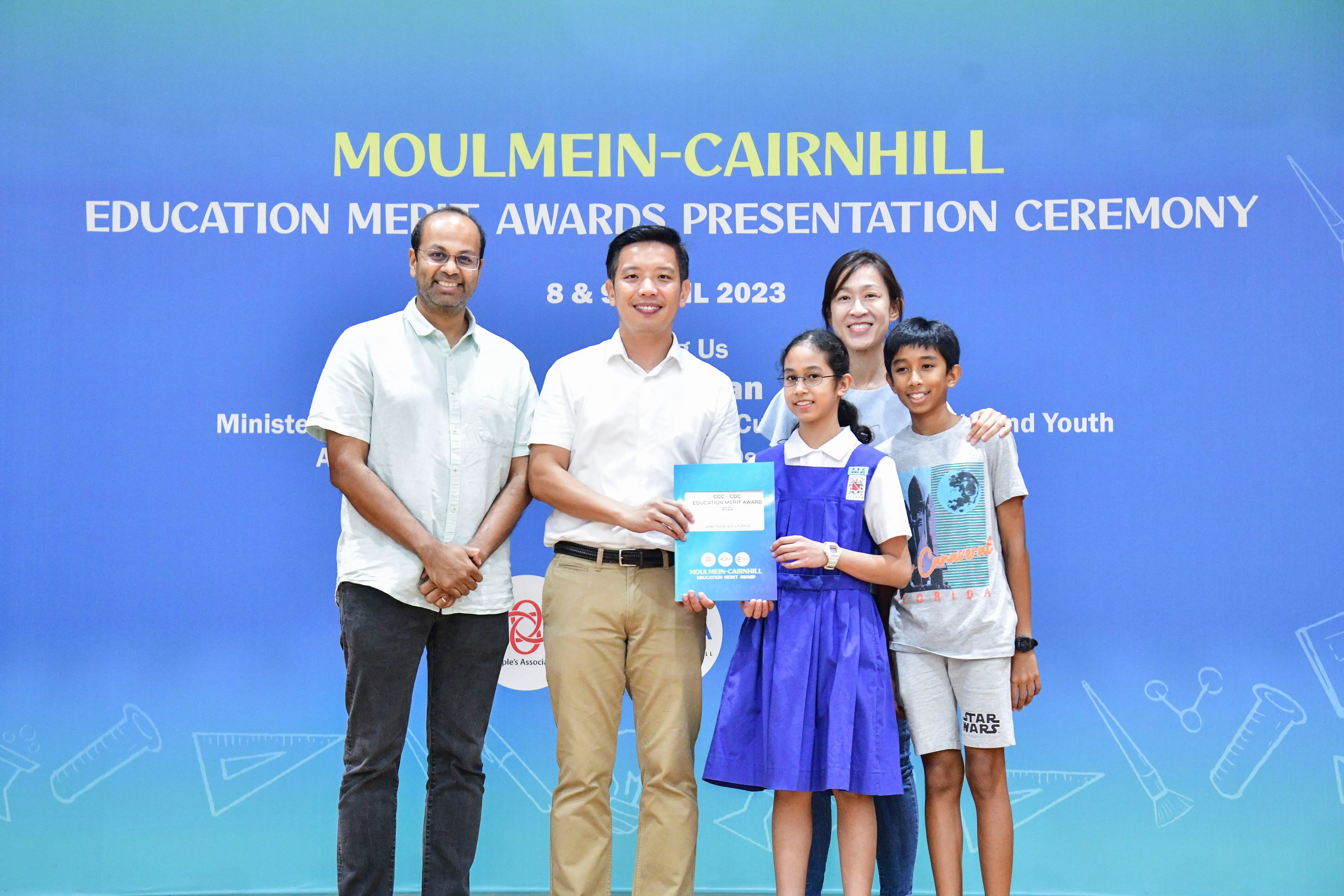 Five people pose at the Moulmein-Cairnhill Education Merit Awards Presentation Ceremony 2023, with a girl holding an award.