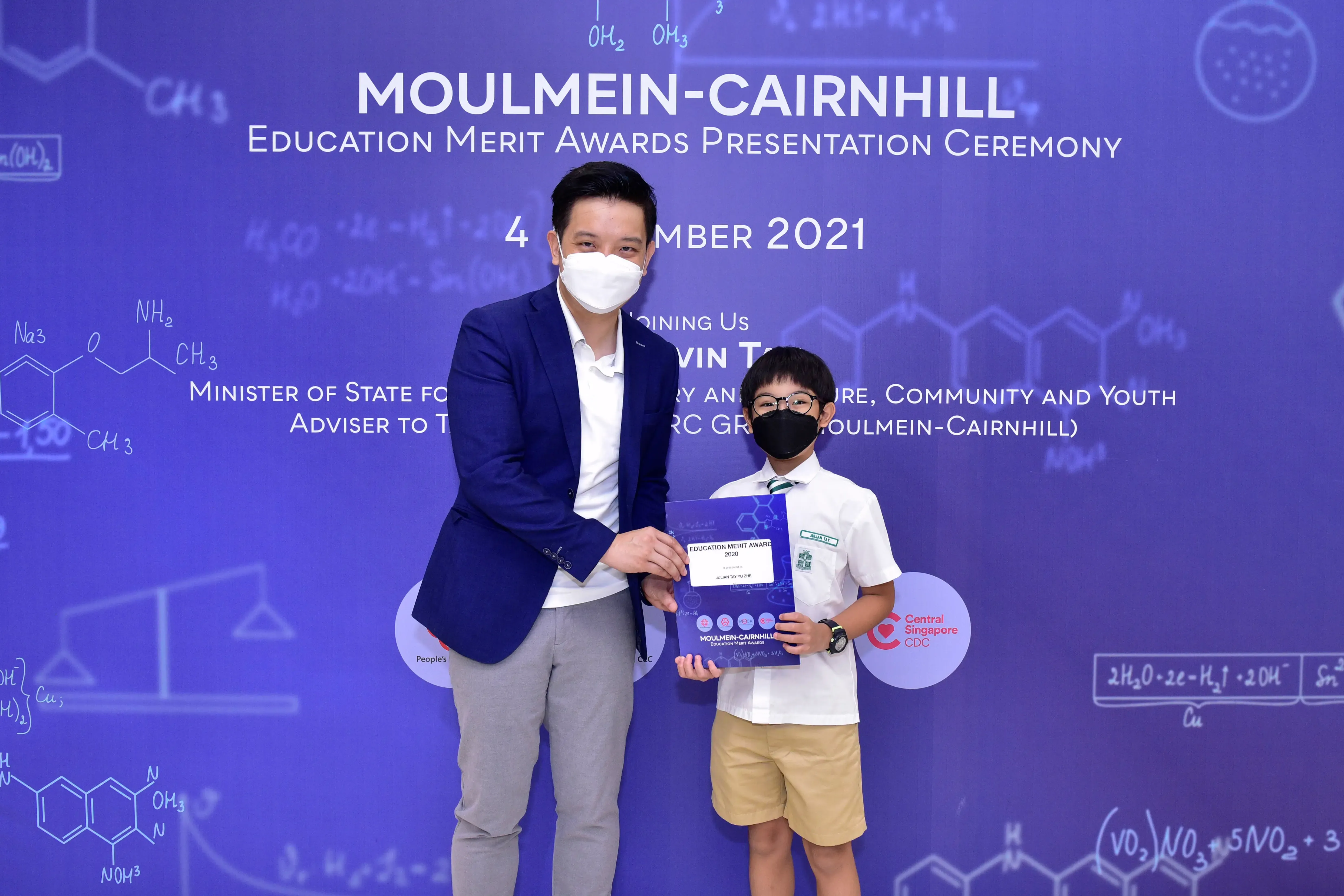 An adult and a masked child hold an award certificate at the Moulmein-Cairnhill Education Merit Awards 2021.
