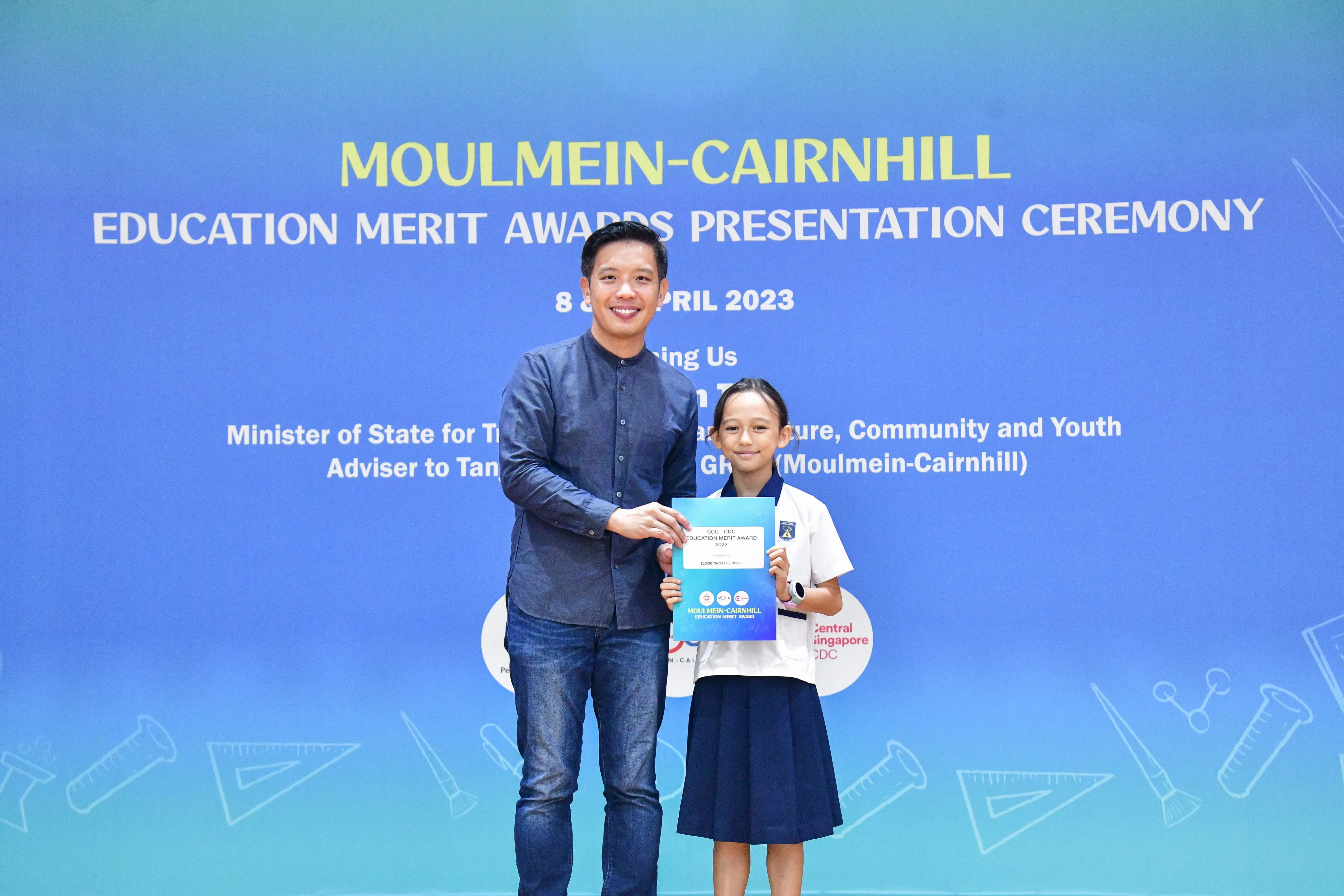 A man and a young girl hold a merit award certificate at the Moulmein-Cairnhill Education Merit Awards Ceremony 2023.
