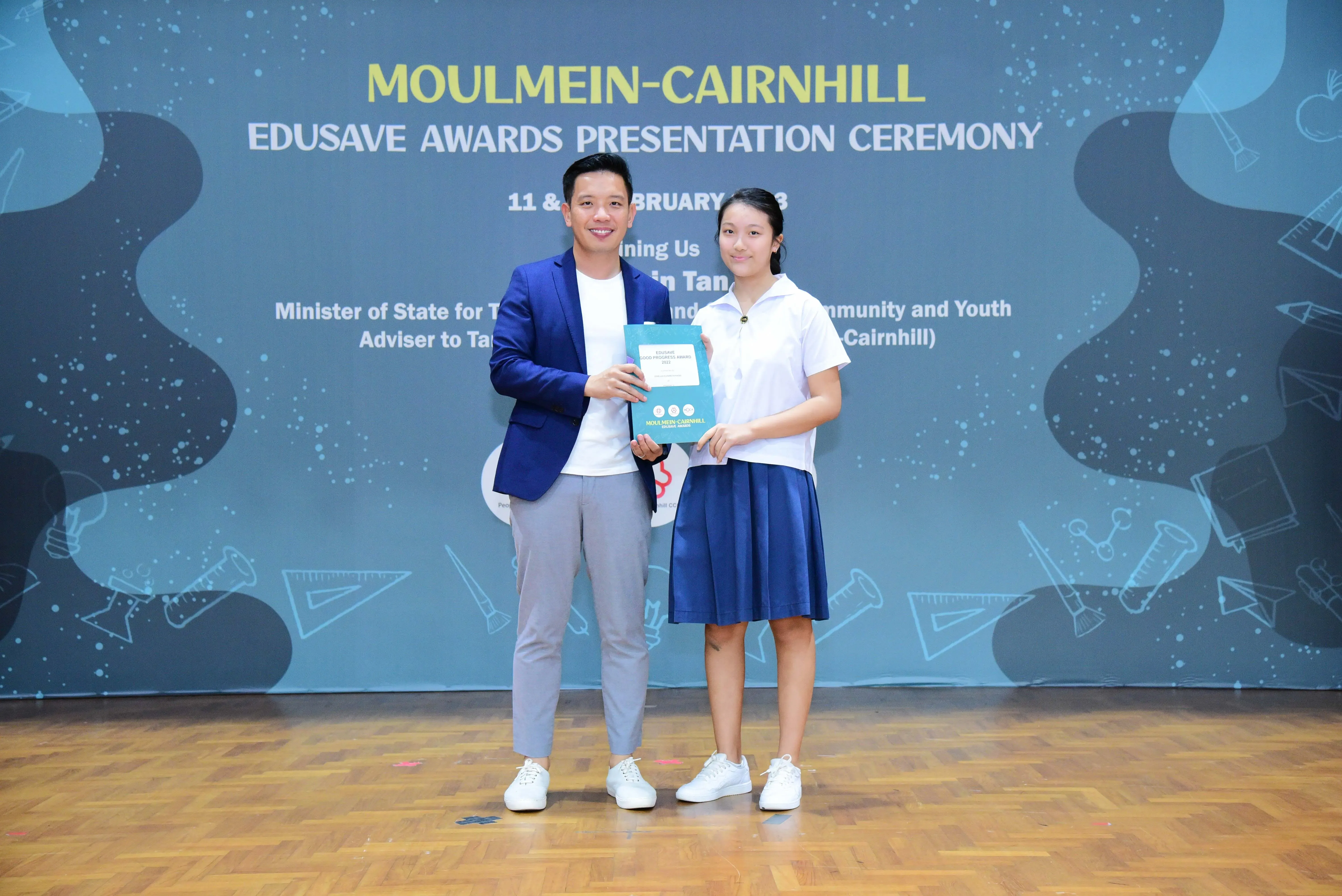 A man in a blue blazer and a girl in school uniform hold an award at the Moulmein-Cairnhill Edusave Awards Ceremony.