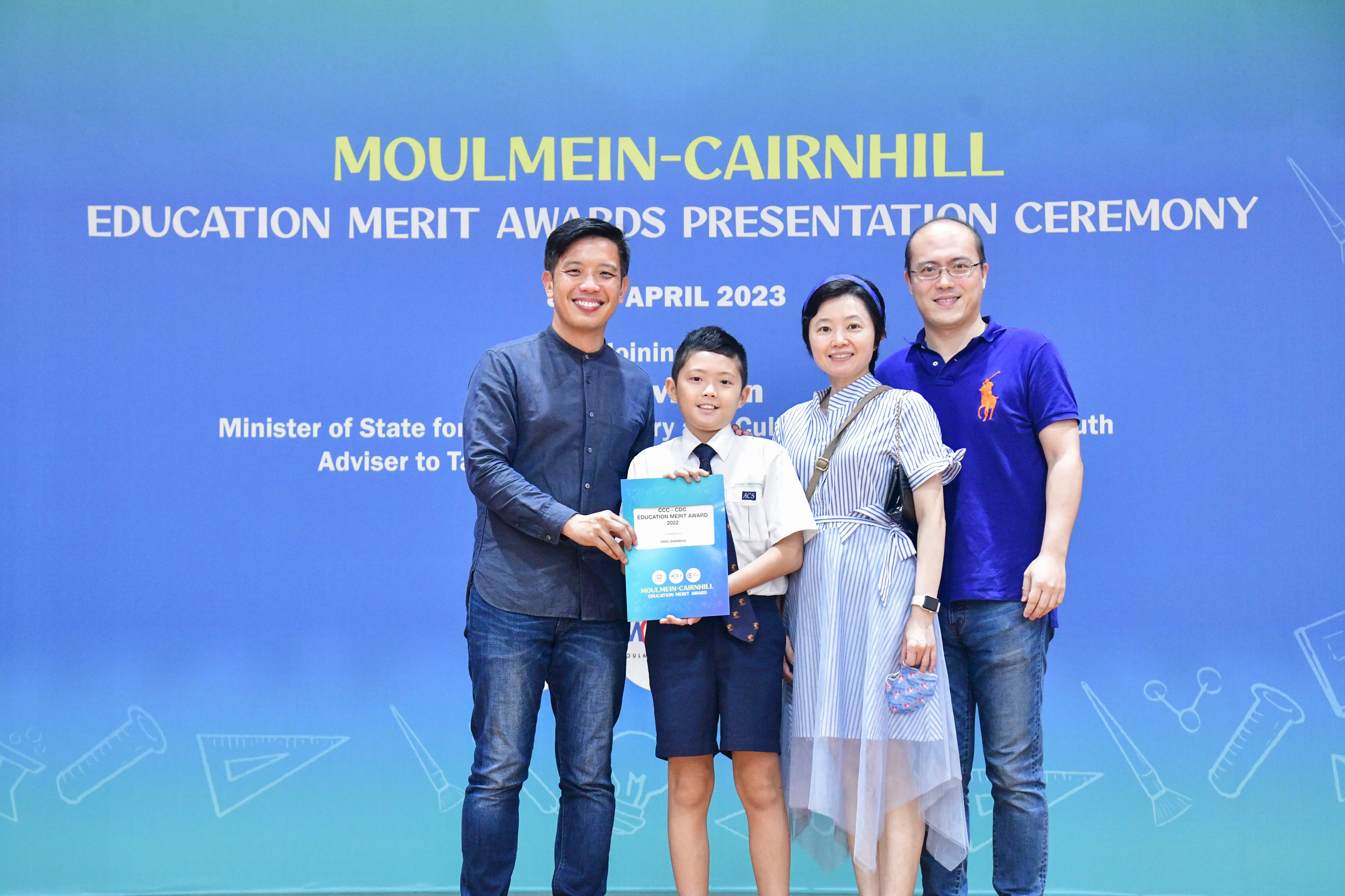 Four people pose at the Moulmein-Cairnhill Education Merit Awards Ceremony April 2023, a boy holding a certificate.