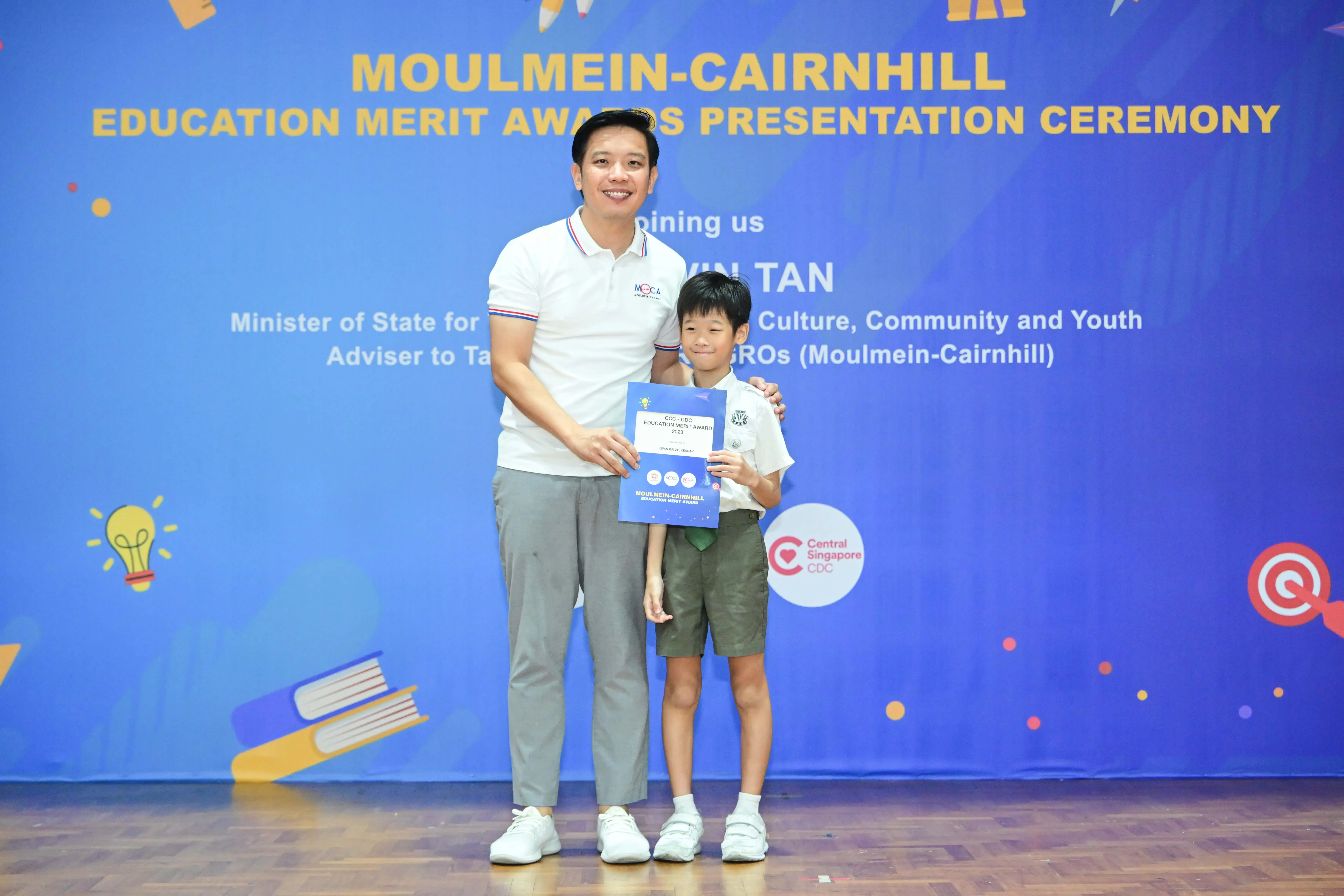 A man and a young boy pose with a certificate at the Moulmein-Cairnhill Education Merit Awards Presentation Ceremony.