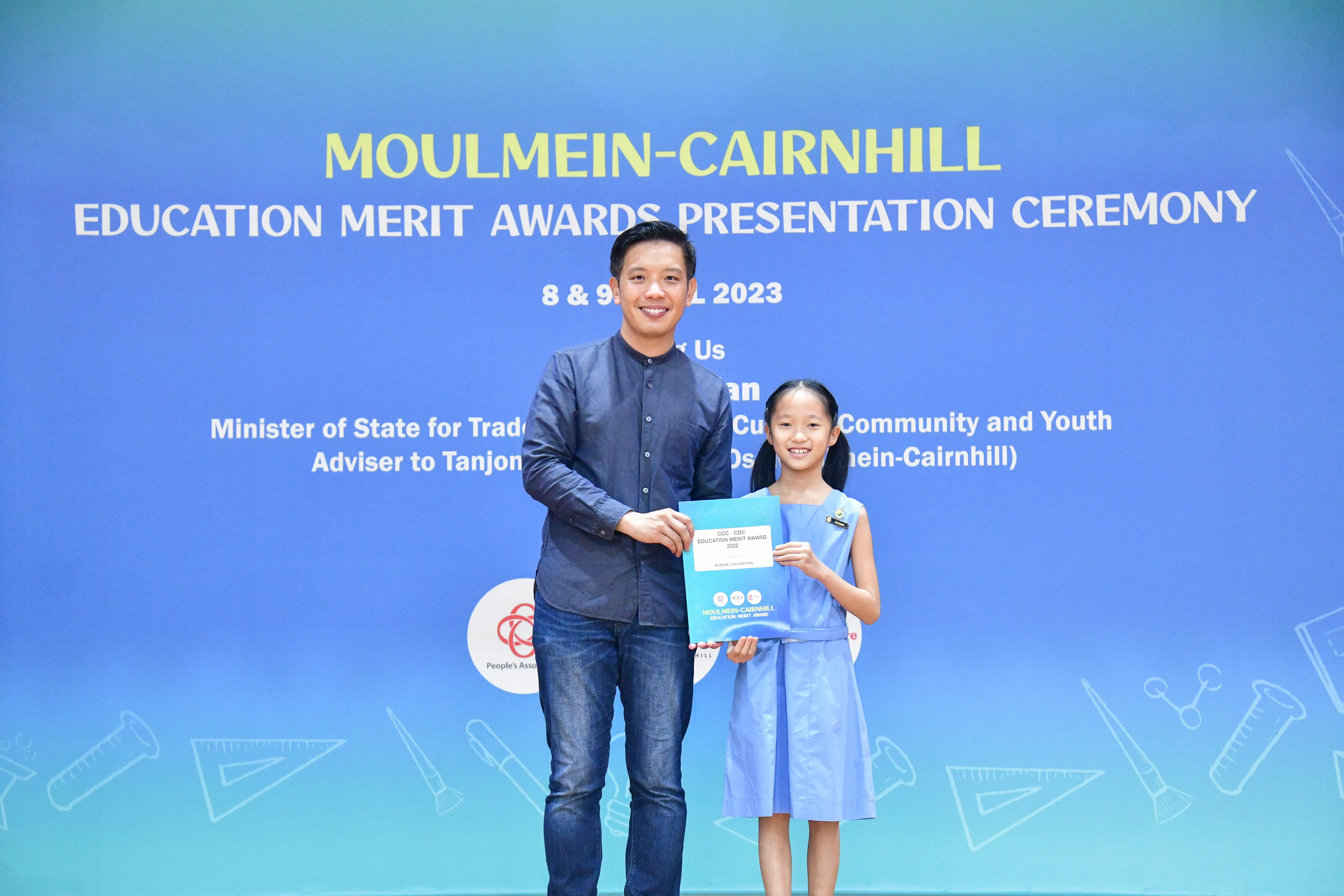 A man and a young girl hold an award certificate at the Moulmein-Cairnhill Education Merit Awards Ceremony 2023.