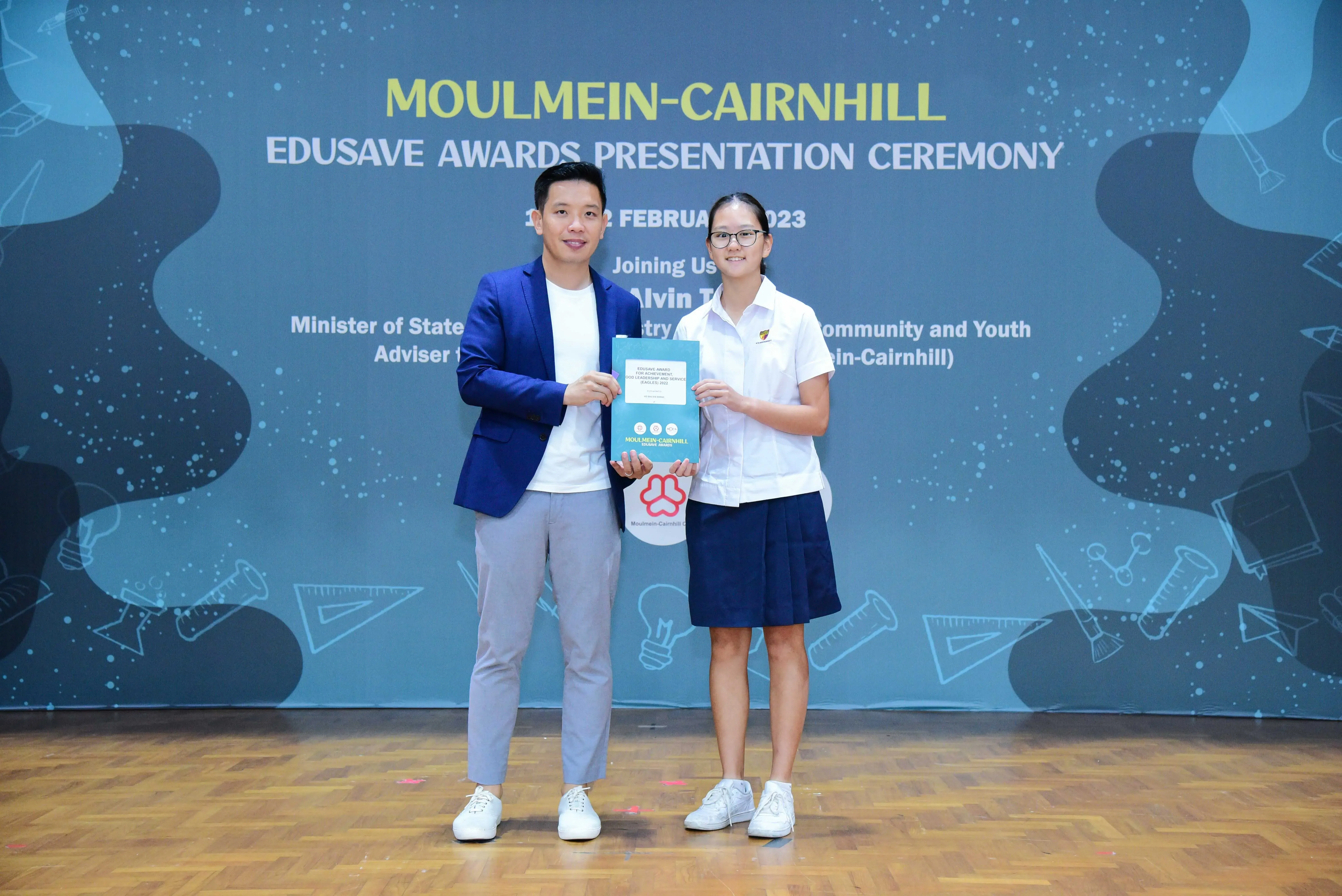 Two people hold a certificate together at the Moulmein-Cairnhill Edusave Awards Presentation Ceremony, February 2023.