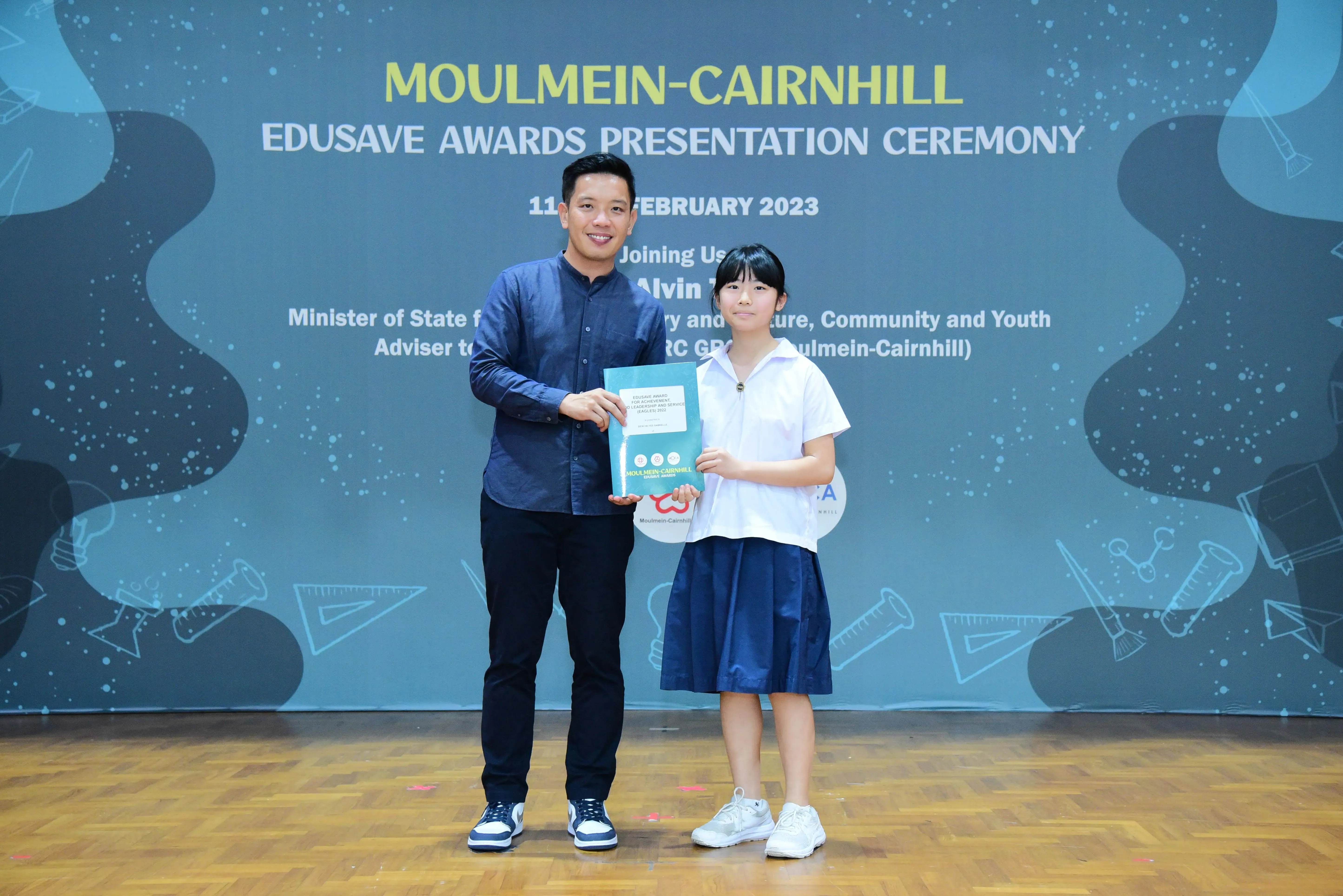 A man and a young girl hold a certificate together at the Moulmein-Cairnhill Edusave Awards Ceremony, February 2023.
