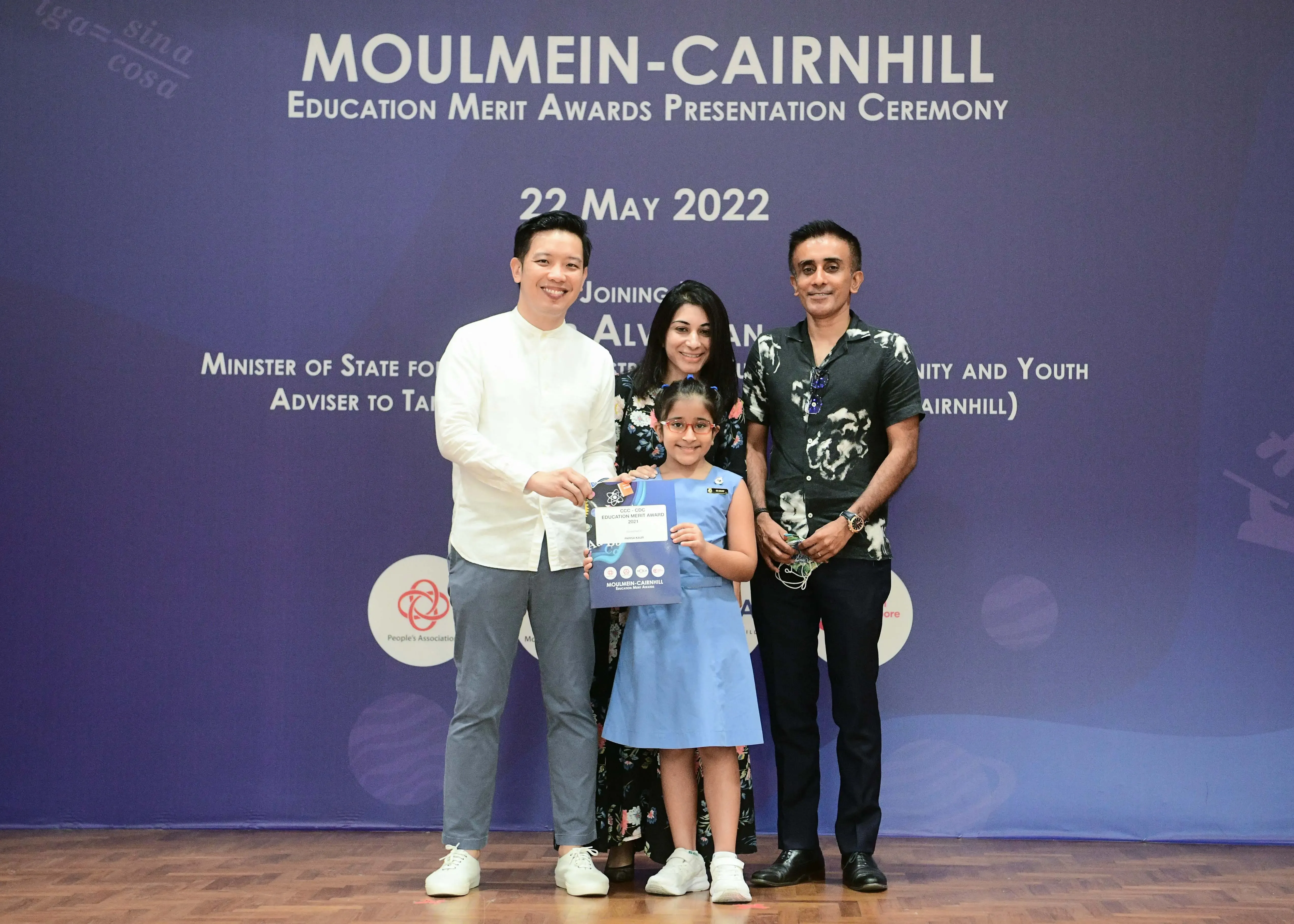 Four people pose at the Moulmein-Cairnhill Education Merit Awards Ceremony on 22 May 2022, with a girl holding a certificate.