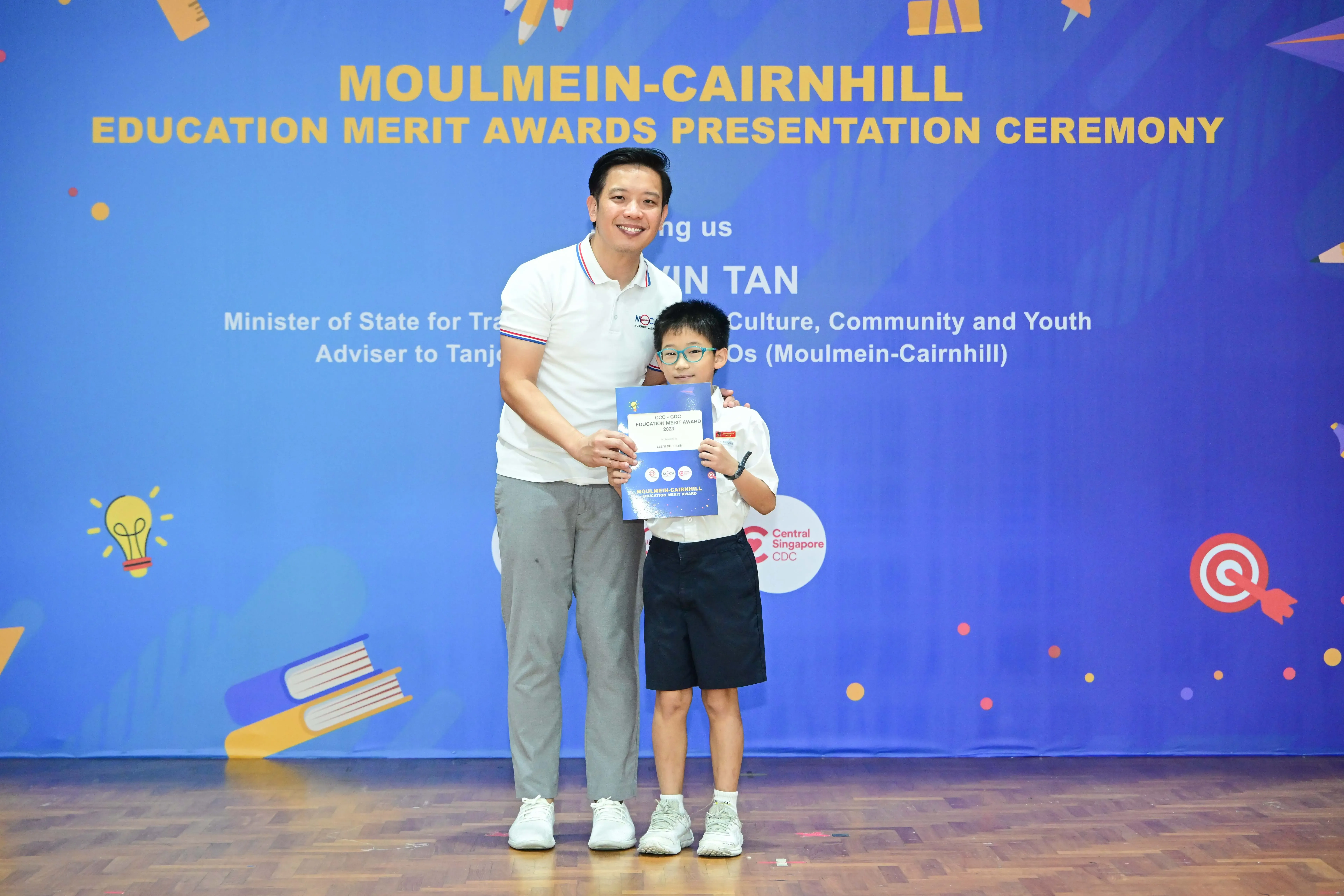 A man and a young boy hold a certificate at the Moulmein-Cairnhill Education Merit Awards Presentation Ceremony.