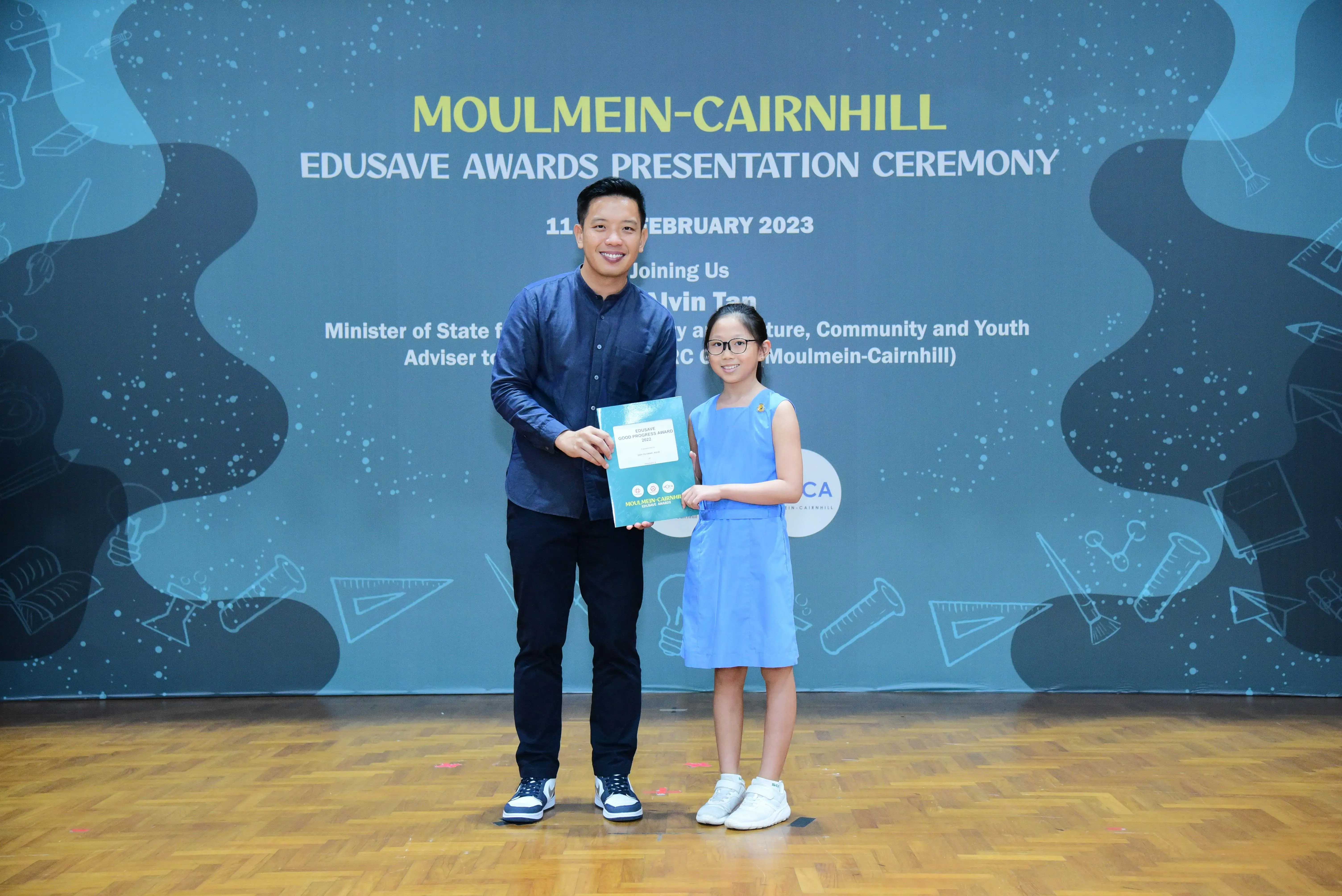 A man and a young girl hold a certificate together at the Moulmein-Cairnhill Edusave Awards Ceremony, February 2023.
