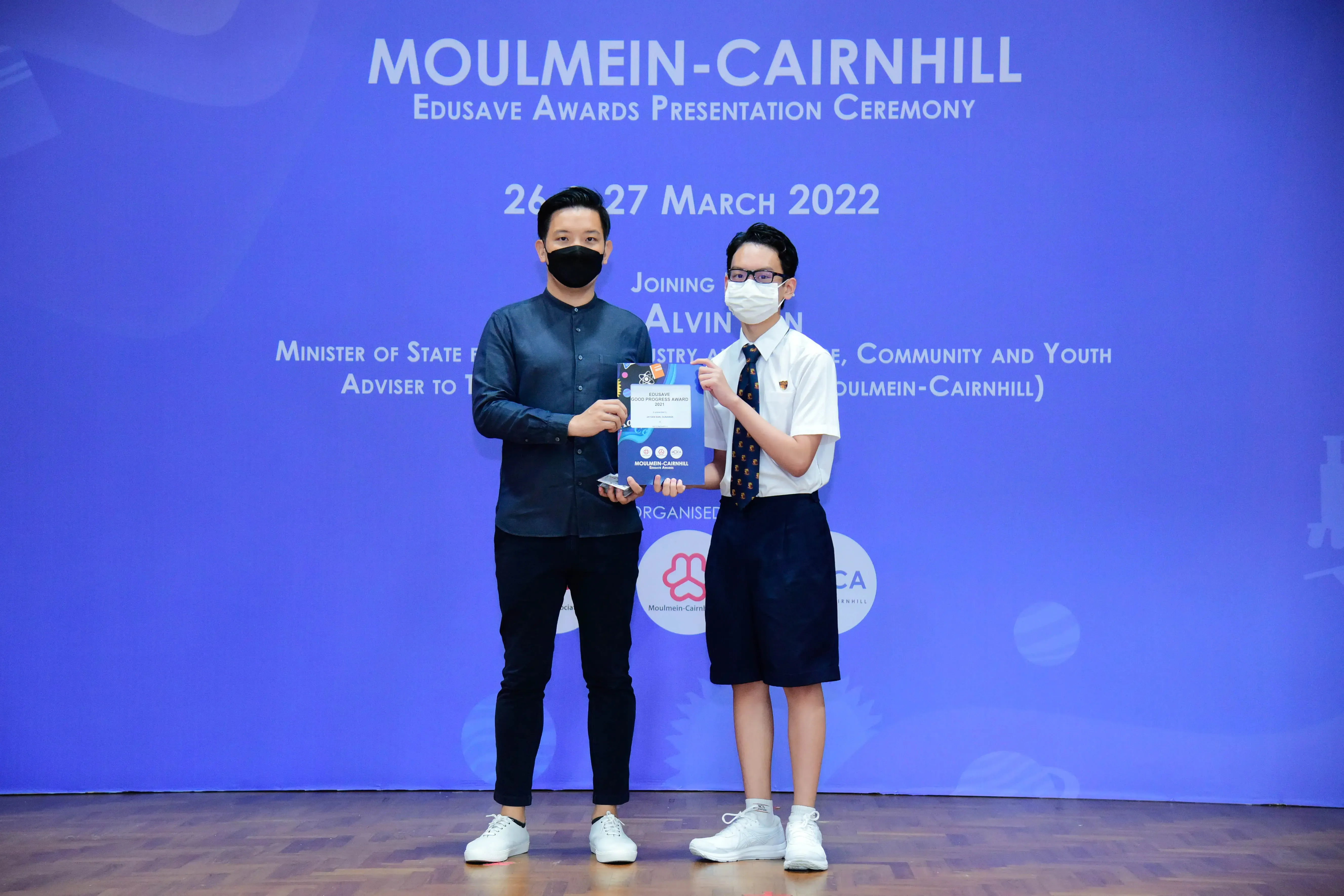 Two masked individuals hold an award certificate at the Moulmein-Cairnhill Edusave Awards Ceremony, March 2022.