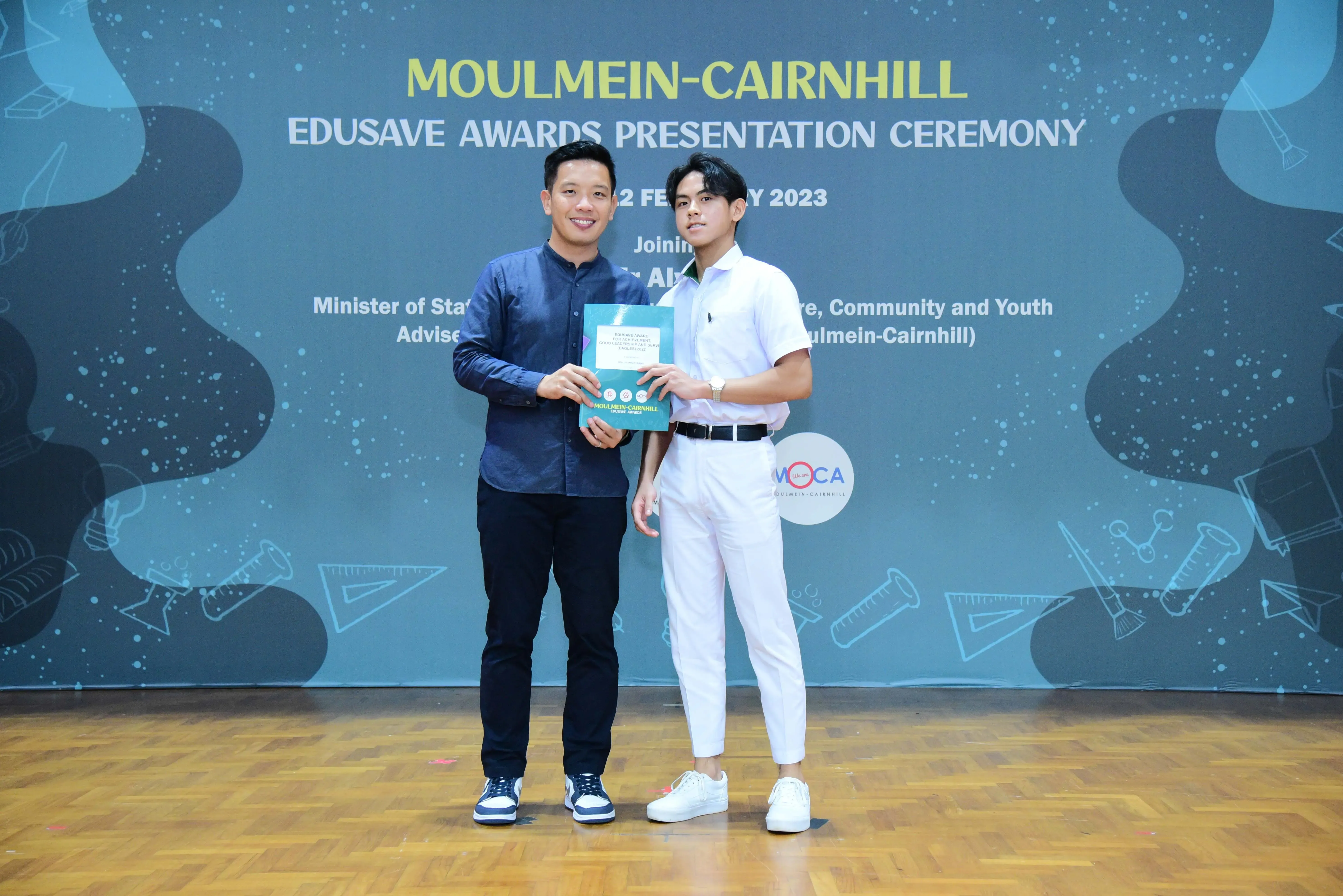 Two men hold a certificate together at the Moulmein-Cairnhill Edusave Awards Presentation Ceremony in 2023.