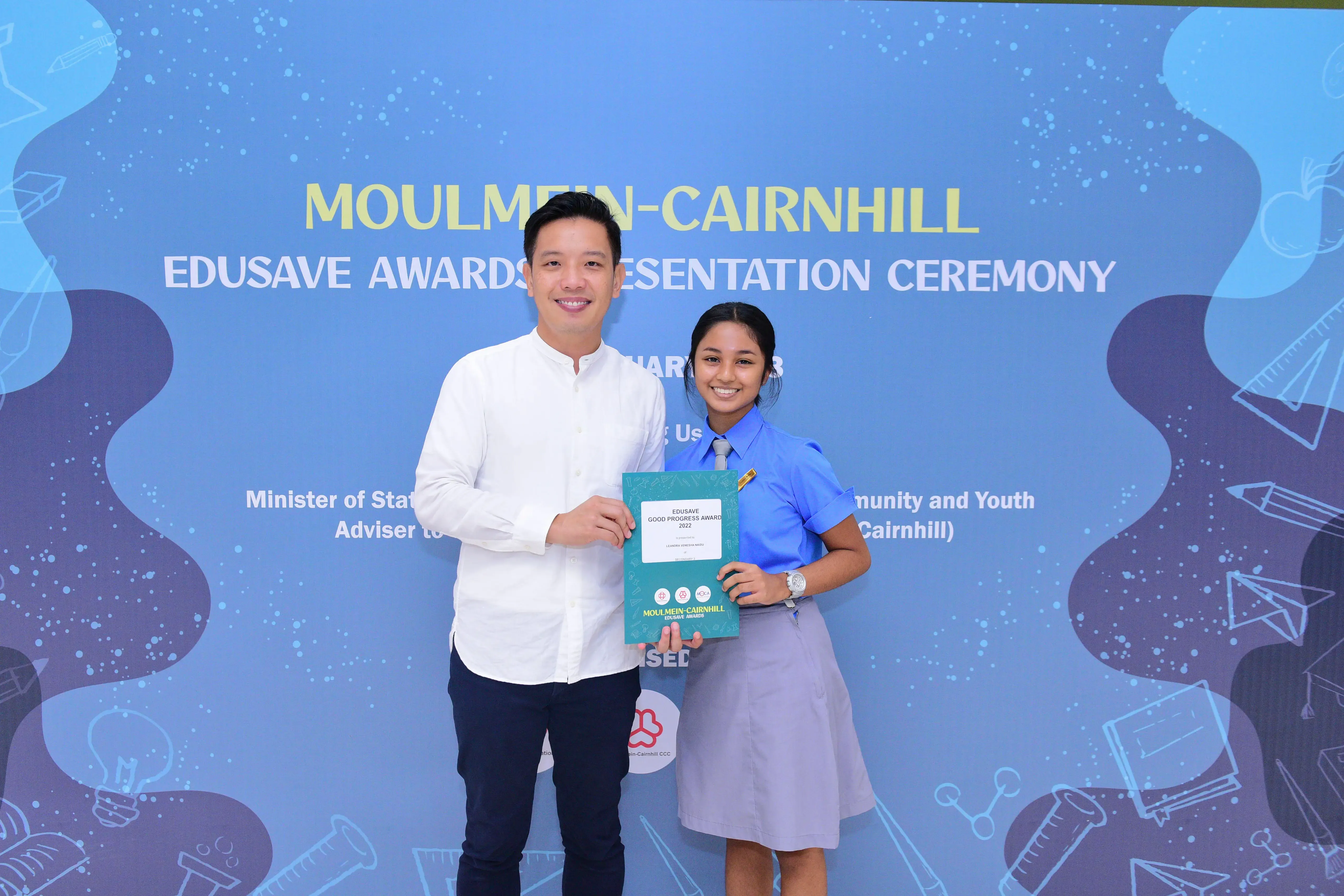 A man and a student in uniform hold an Edusave Good Progress Award at the Moulmein-Cairnhill Awards Ceremony.