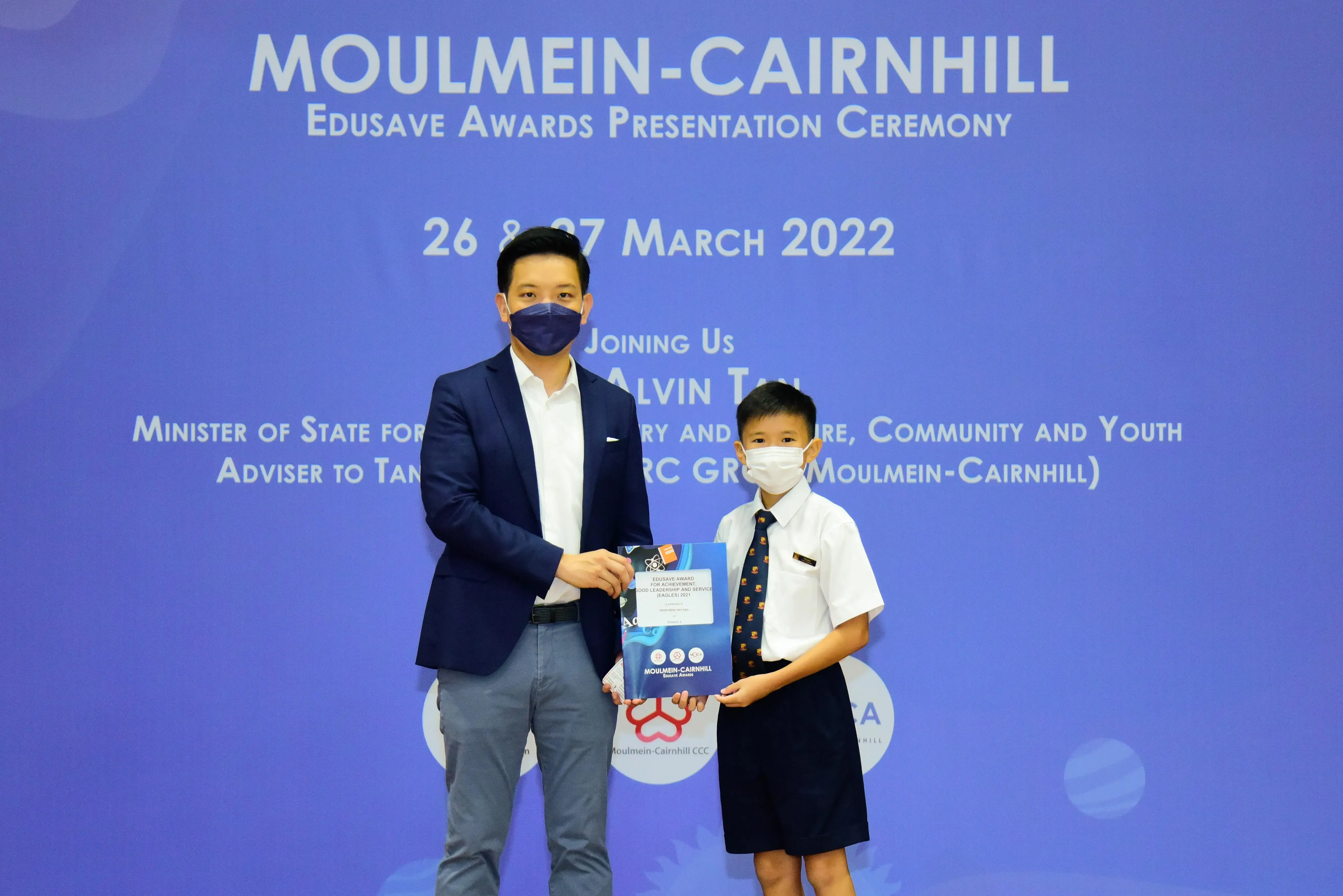 An adult and a young student in uniform hold an award together at the Moulmein-Cairnhill Edusave Awards Ceremony 2022.