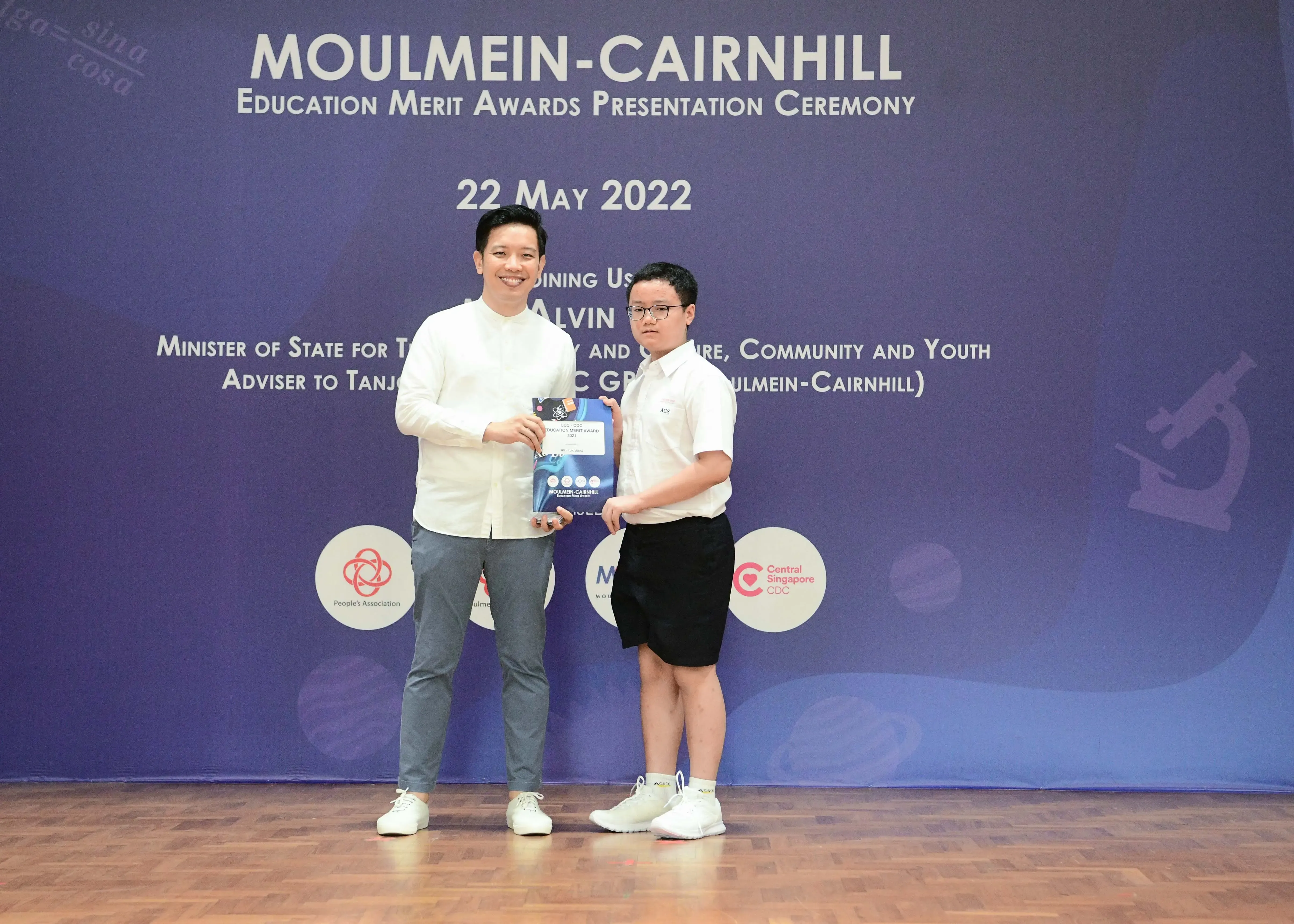 Two people hold an award together at the Moulmein-Cairnhill Education Merit Awards Presentation Ceremony on 22 May 2022.