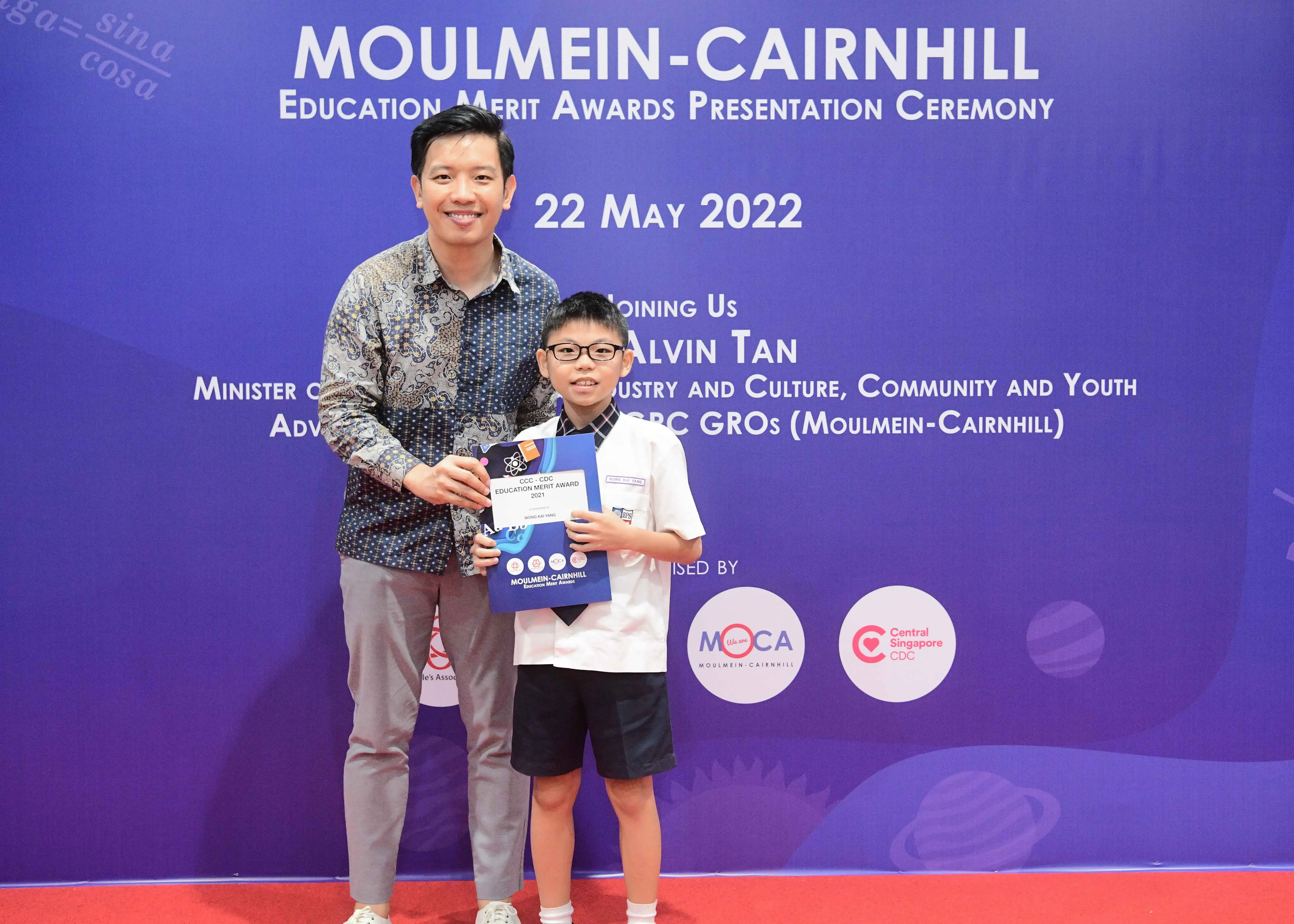 A man and a young boy holding an award certificate at the Moulmein-Cairnhill Education Merit Awards ceremony on 22 May 2022.