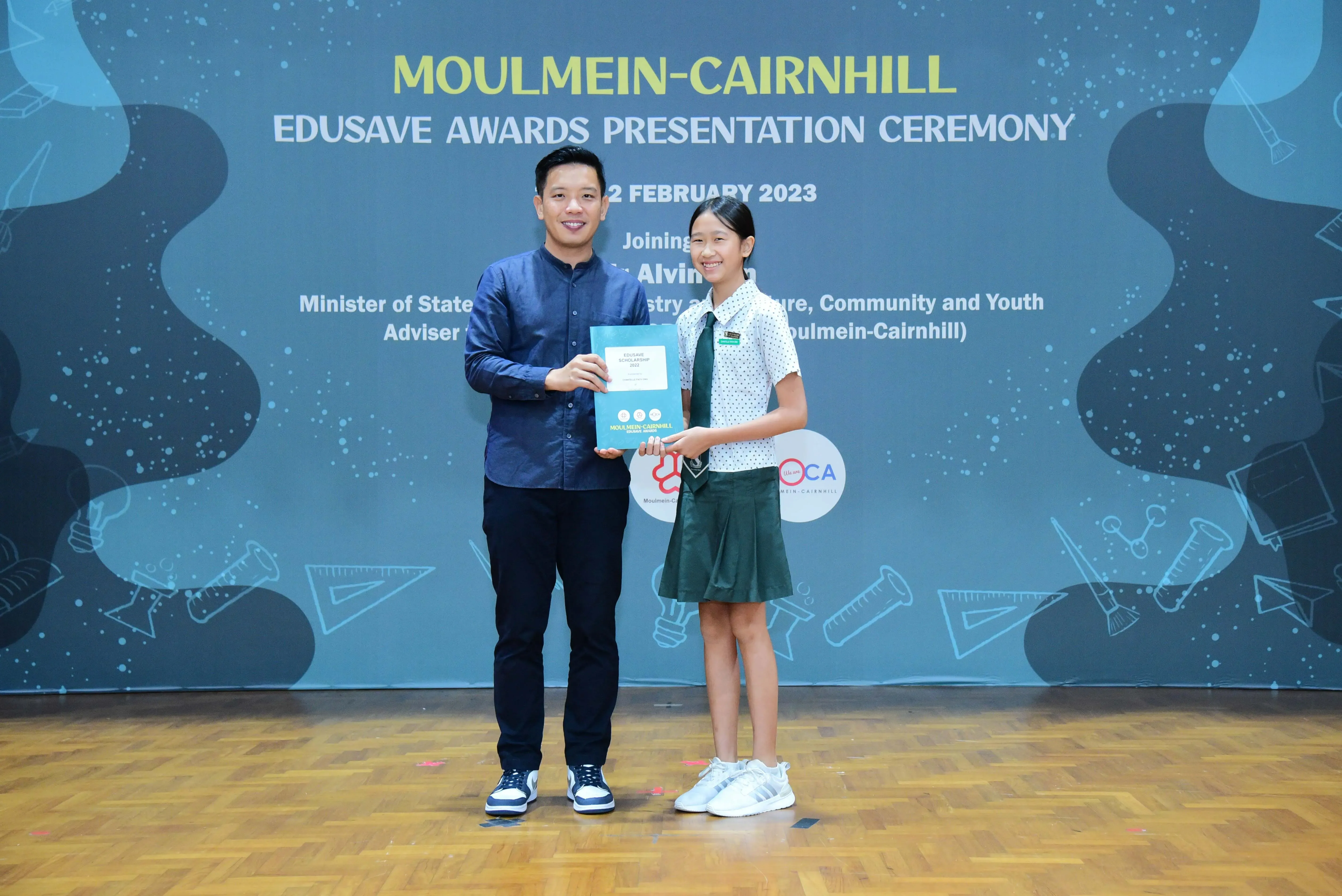 A man and a young girl hold a certificate together at the Moulmein-Cairnhill Edusave Awards Ceremony, February 2023.