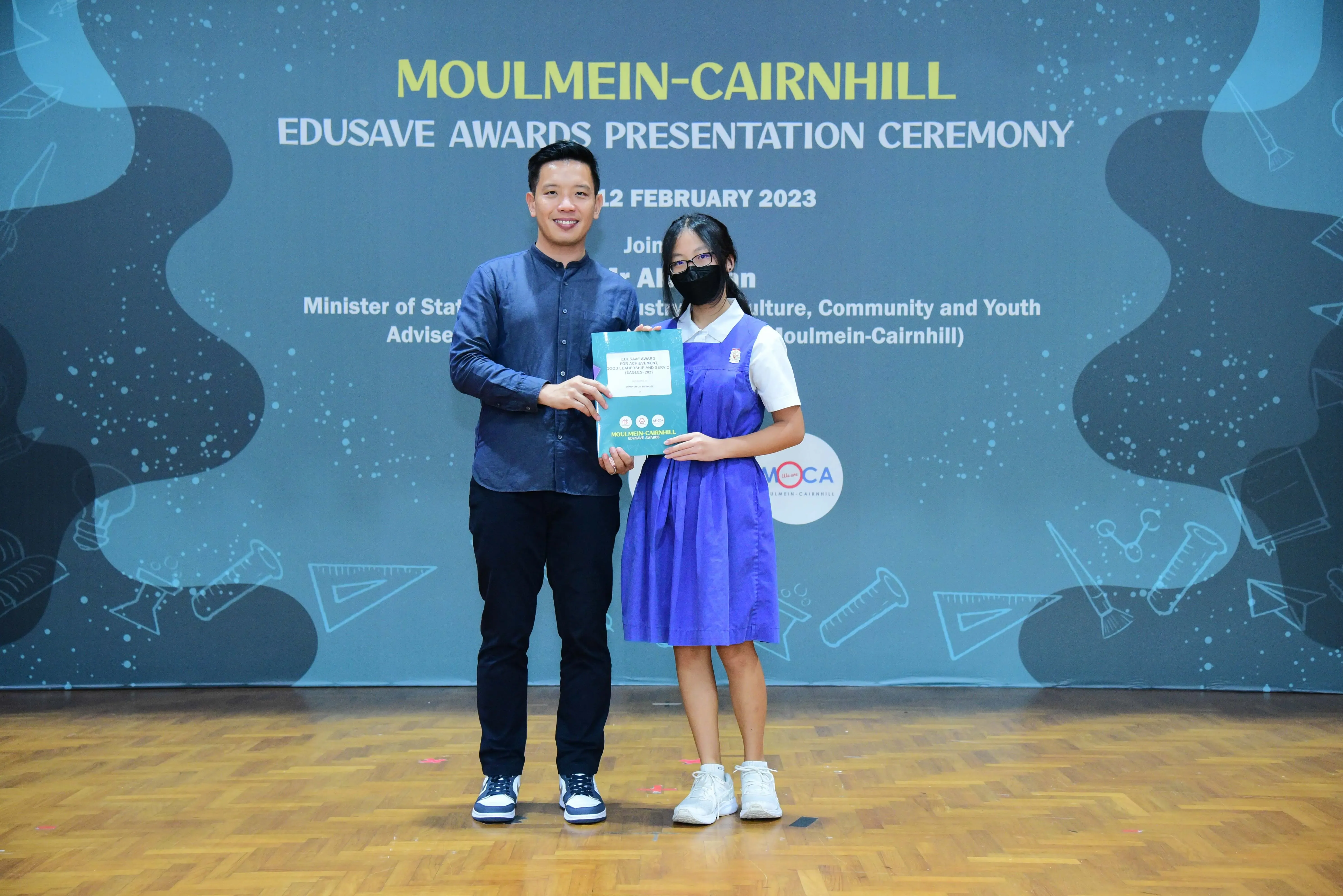 A man and a schoolgirl hold a certificate at the Moulmein-Cairnhill Edusave Awards Ceremony on 12 February 2023.