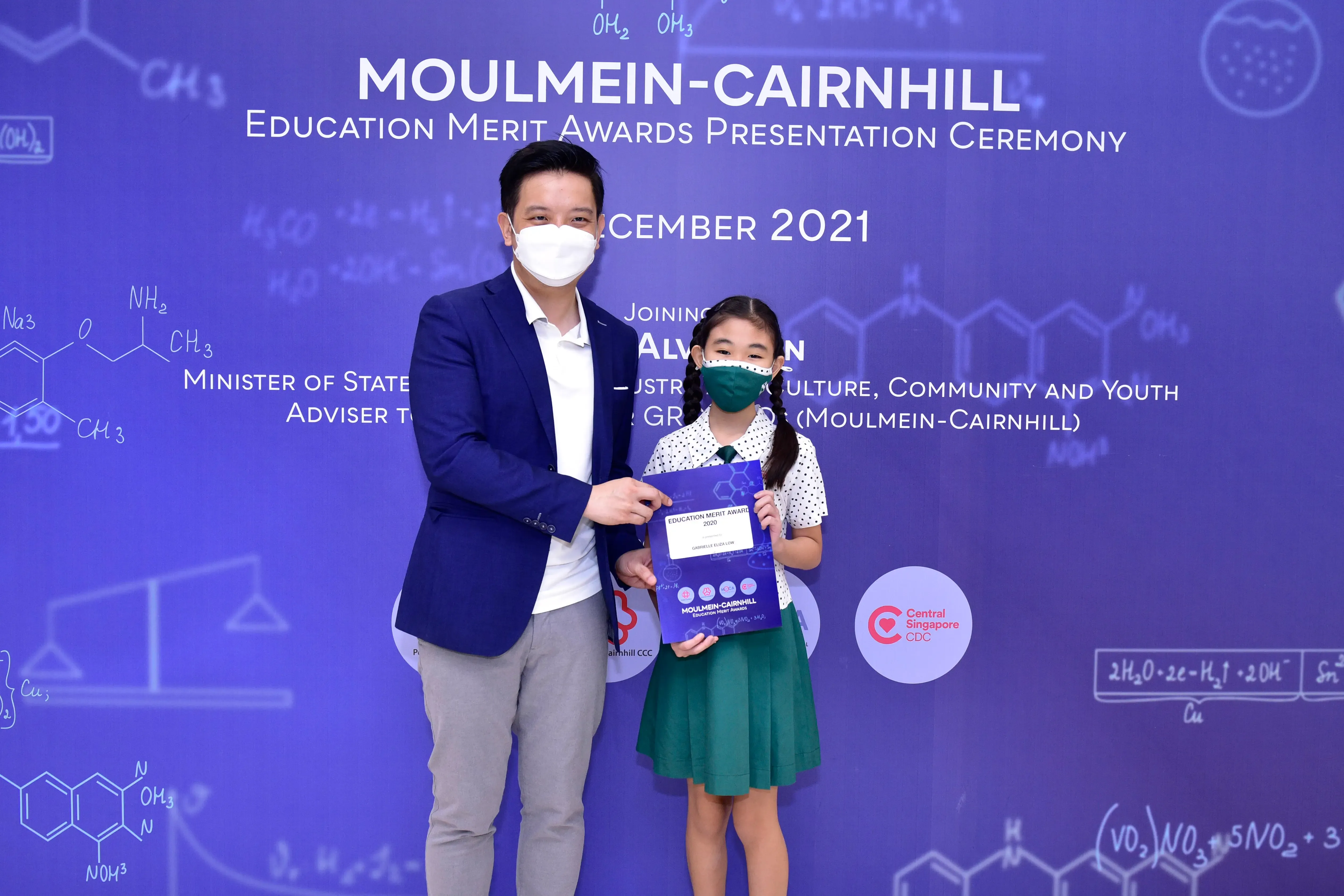 A man and a young girl wearing masks hold an award certificate at the Moulmein-Cairnhill Education Merit Awards 2021.