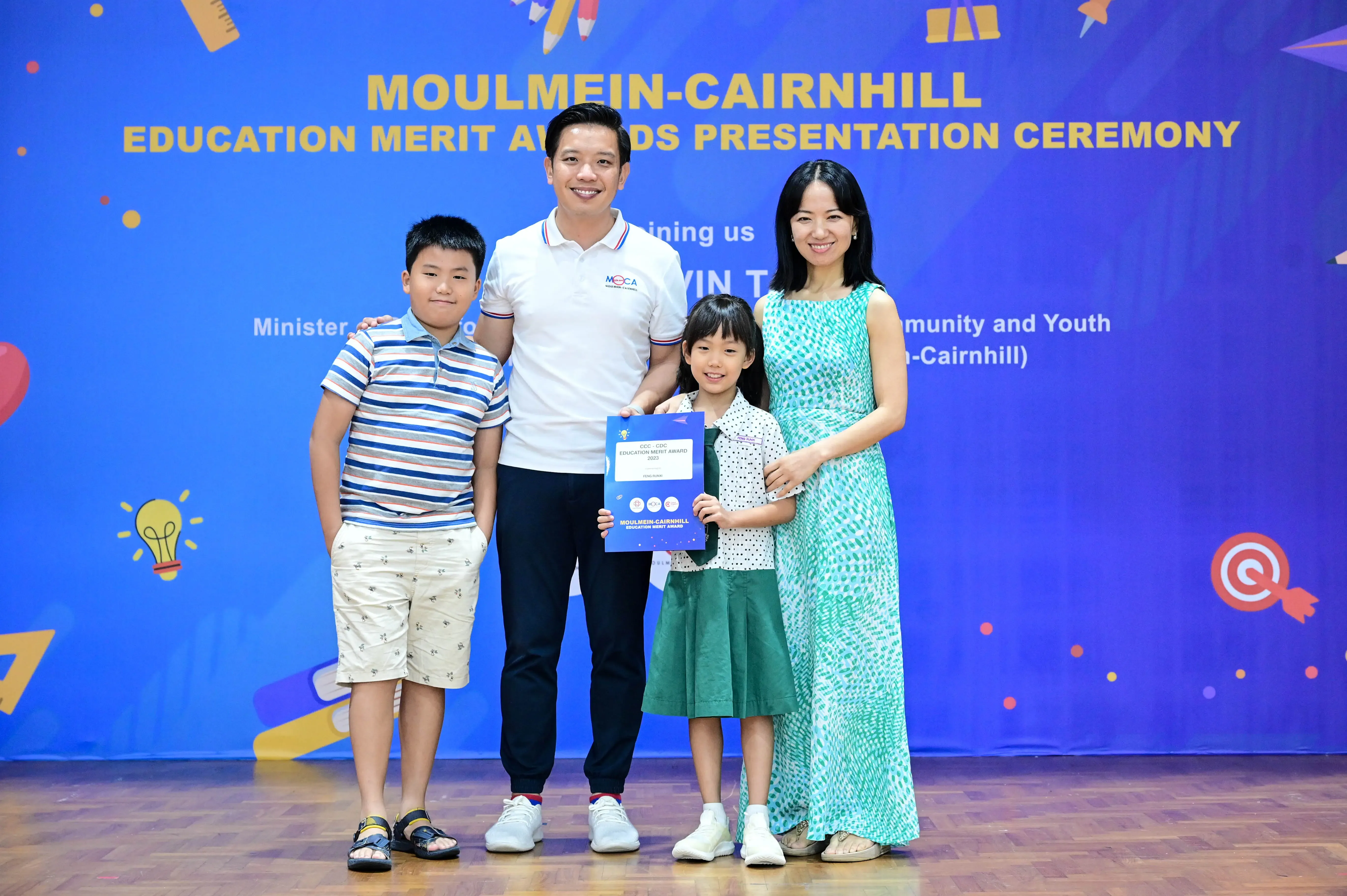 Two adults and two children pose with a certificate at the Moulmein-Cairnhill Education Merit Awards Presentation Ceremony.