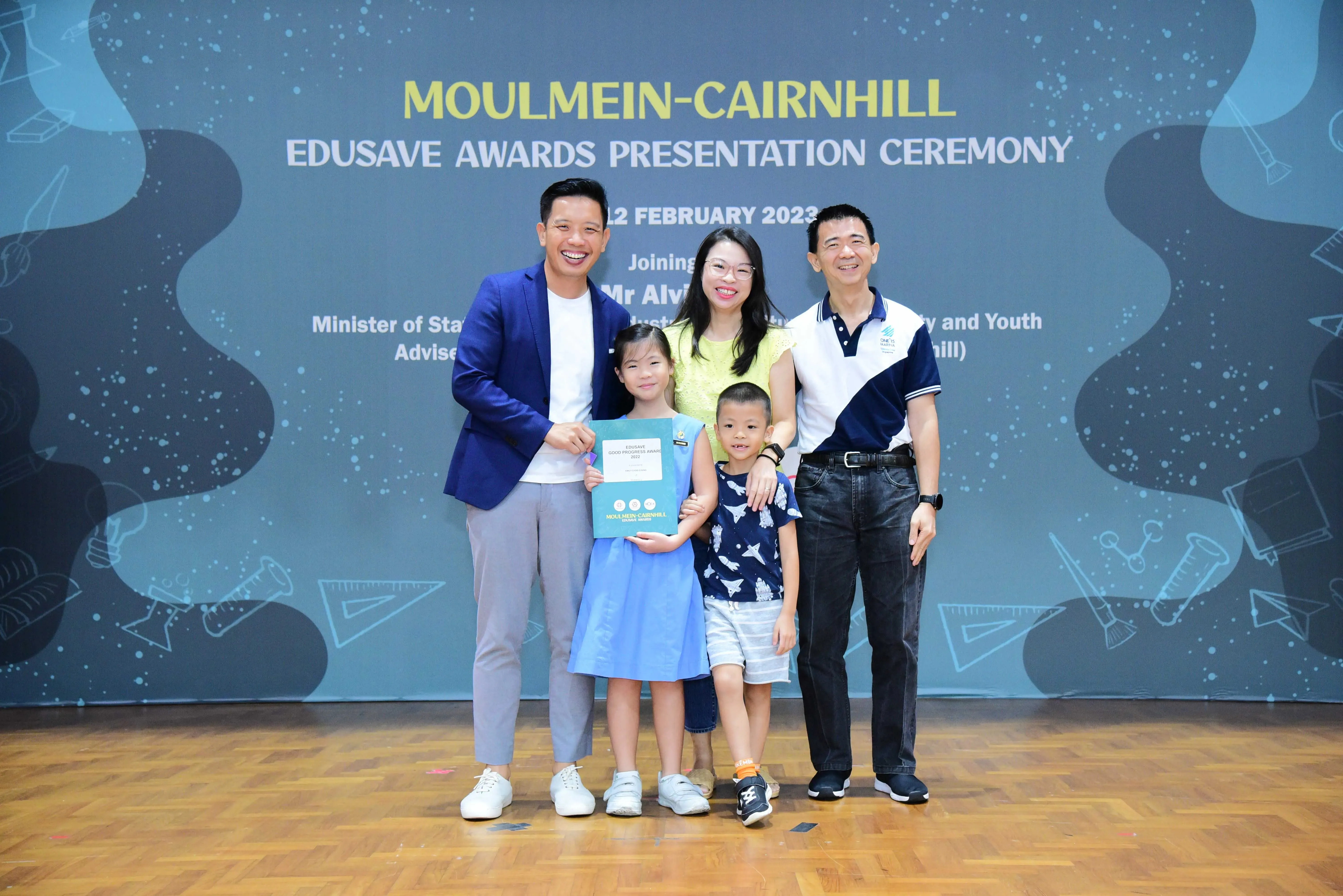 Five people pose at the Moulmein-Cairnhill Edusave Awards Presentation Ceremony; a girl holds a certificate.