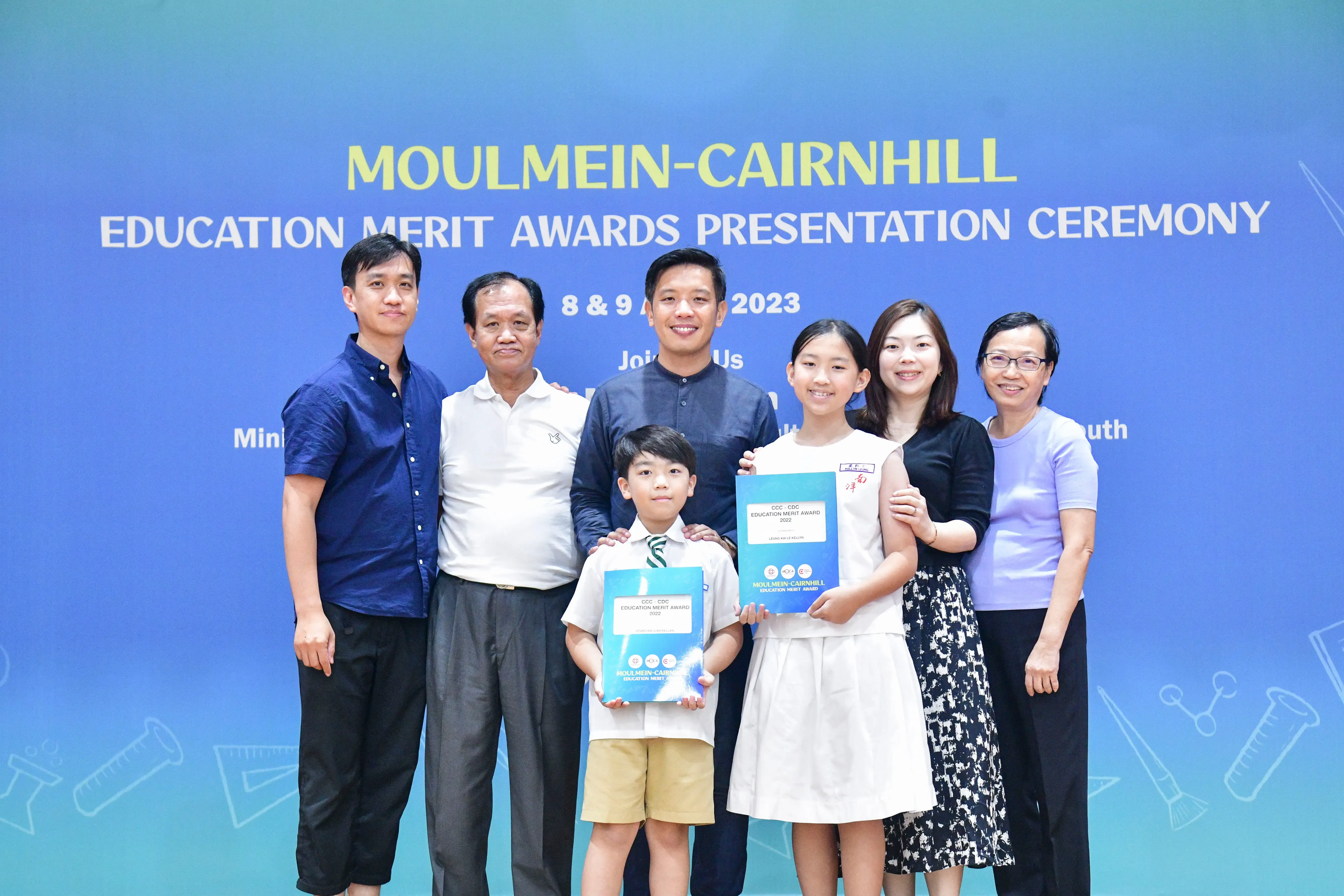 Six adults and two children pose with award booklets at the Moulmein-Cairnhill Education Merit Awards Ceremony 2023.