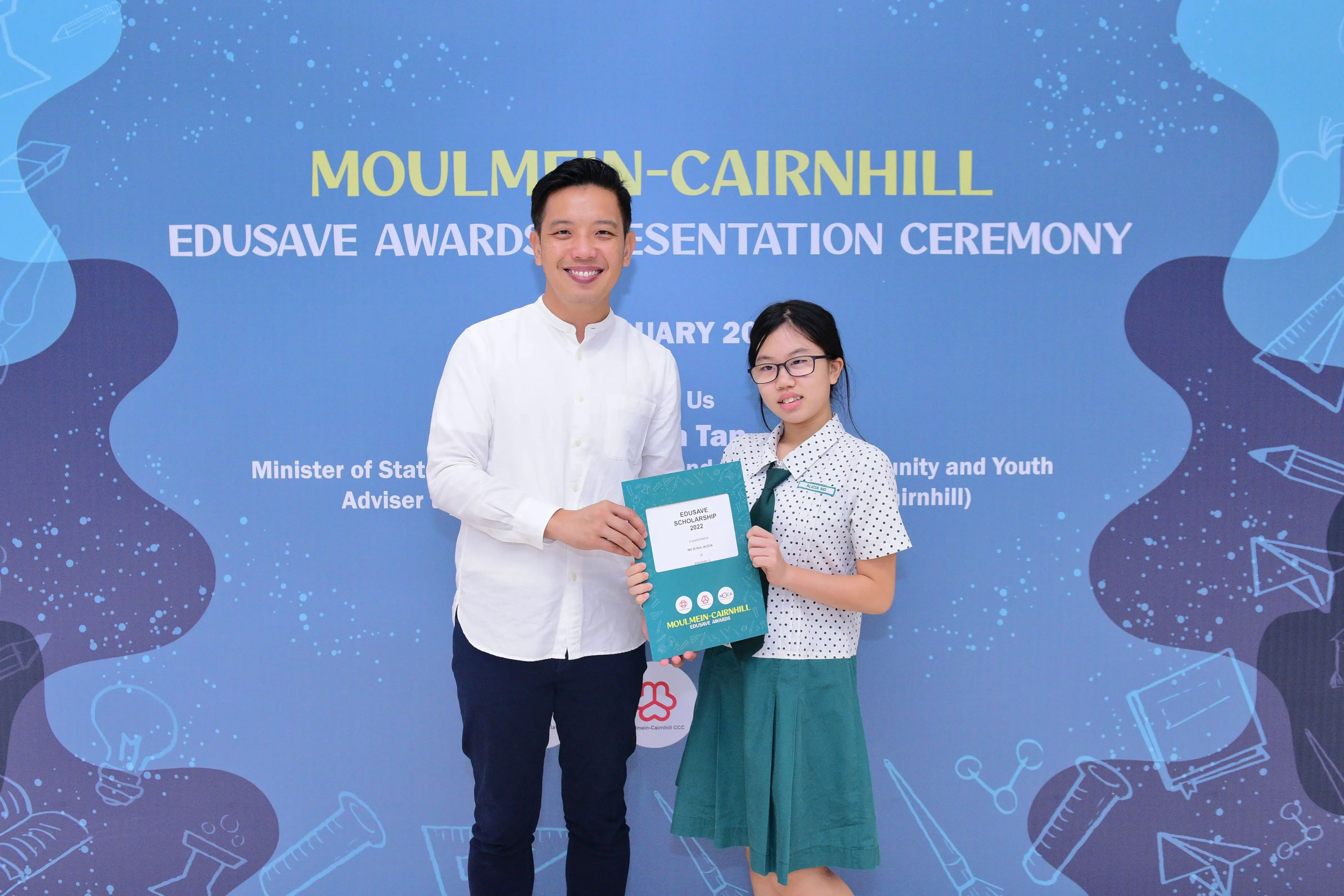 A man and a young girl hold an Edusave scholarship certificate at the Moulmein-Cairnhill Awards Ceremony.