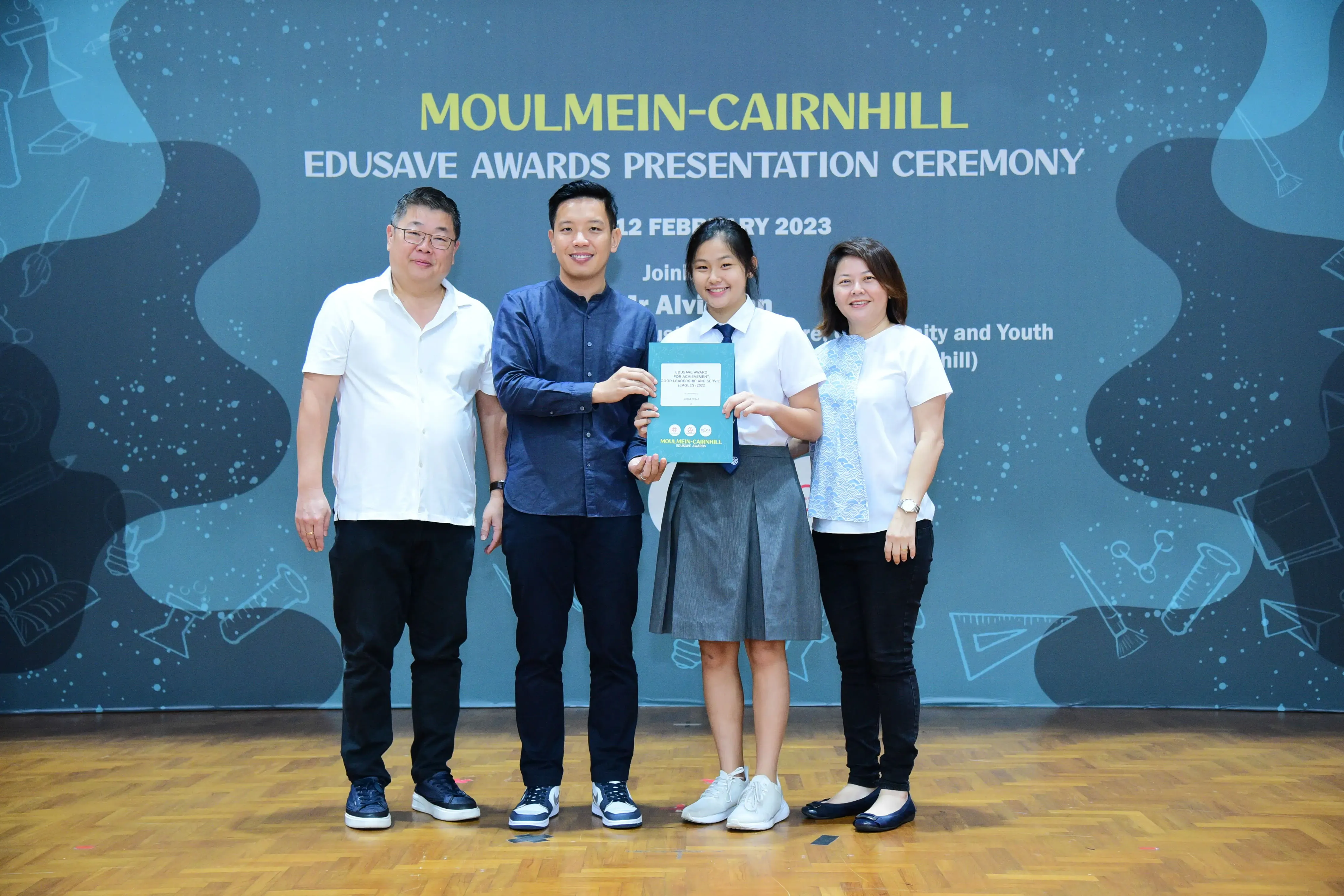 Four people pose together at the Moulmein-Cairnhill Edusave Awards Presentation Ceremony, holding a certificate.