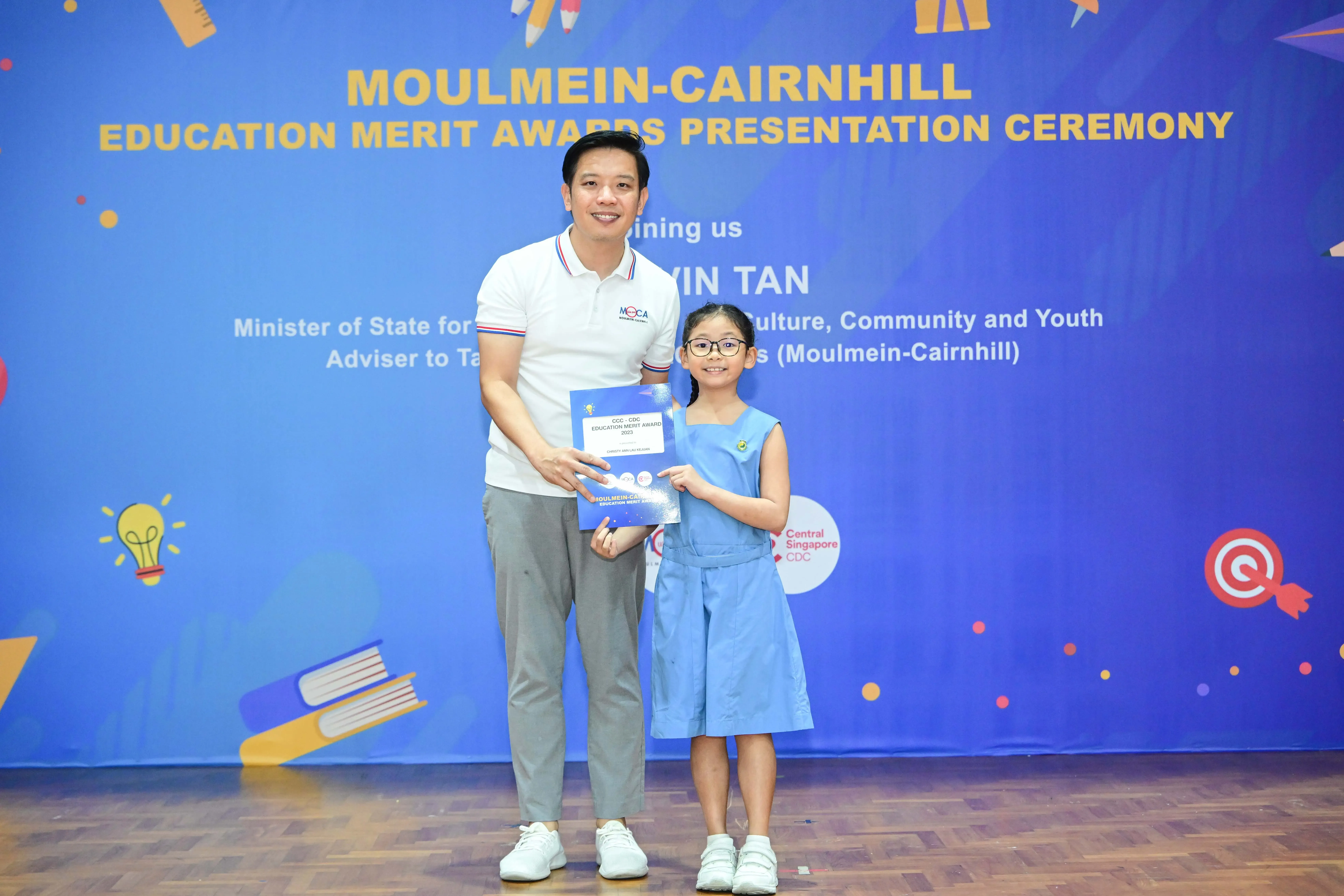 A man and a young girl hold an award certificate at the Moulmein-Cairnhill Education Merit Awards Presentation Ceremony.