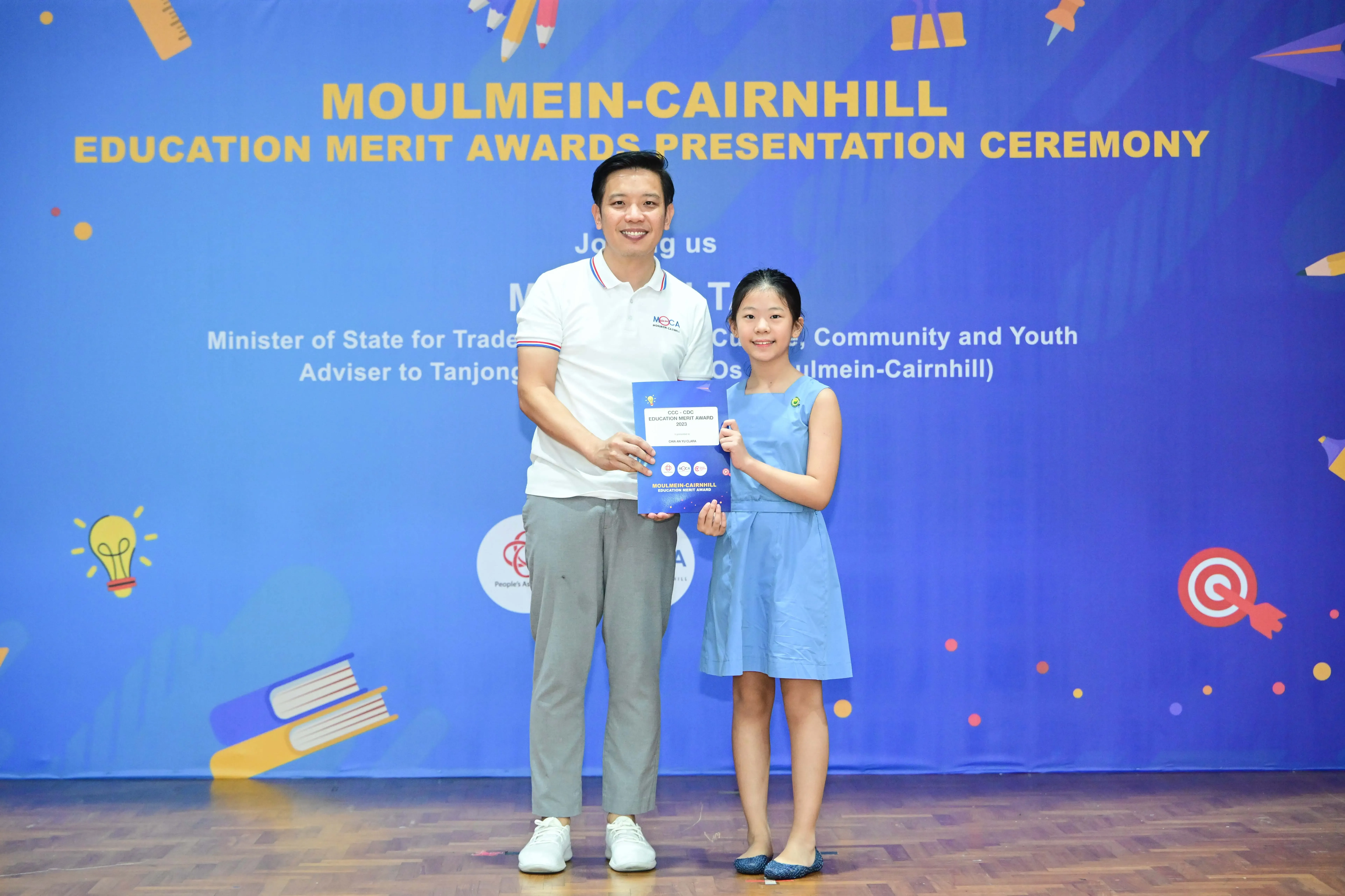 A man and a young girl hold an award certificate at the Moulmein-Cairnhill Education Merit Awards Presentation Ceremony.