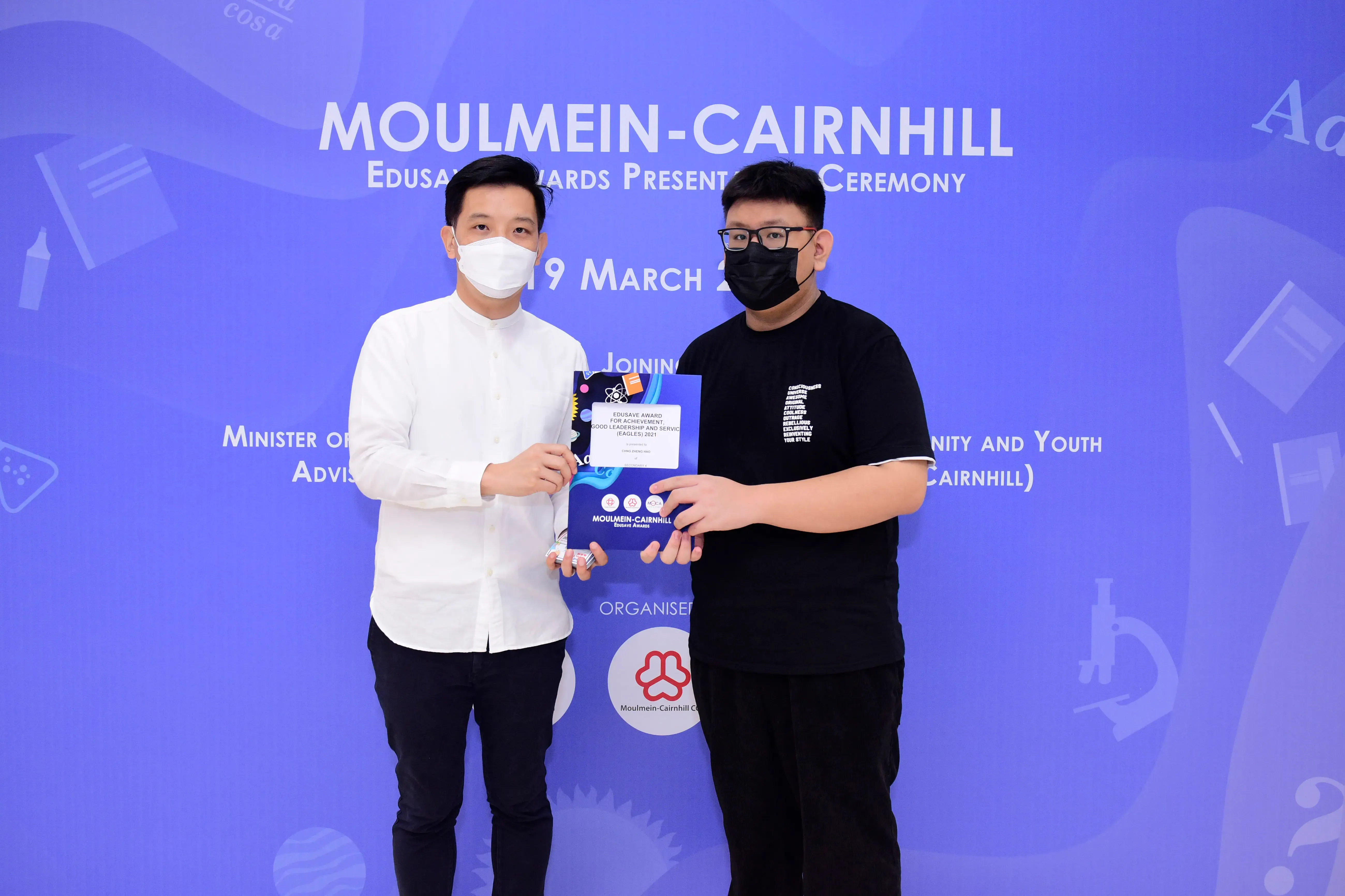 Two masked men hold an award certificate at the Moulmein-Cairnhill Edusave Awards Presentation Ceremony.