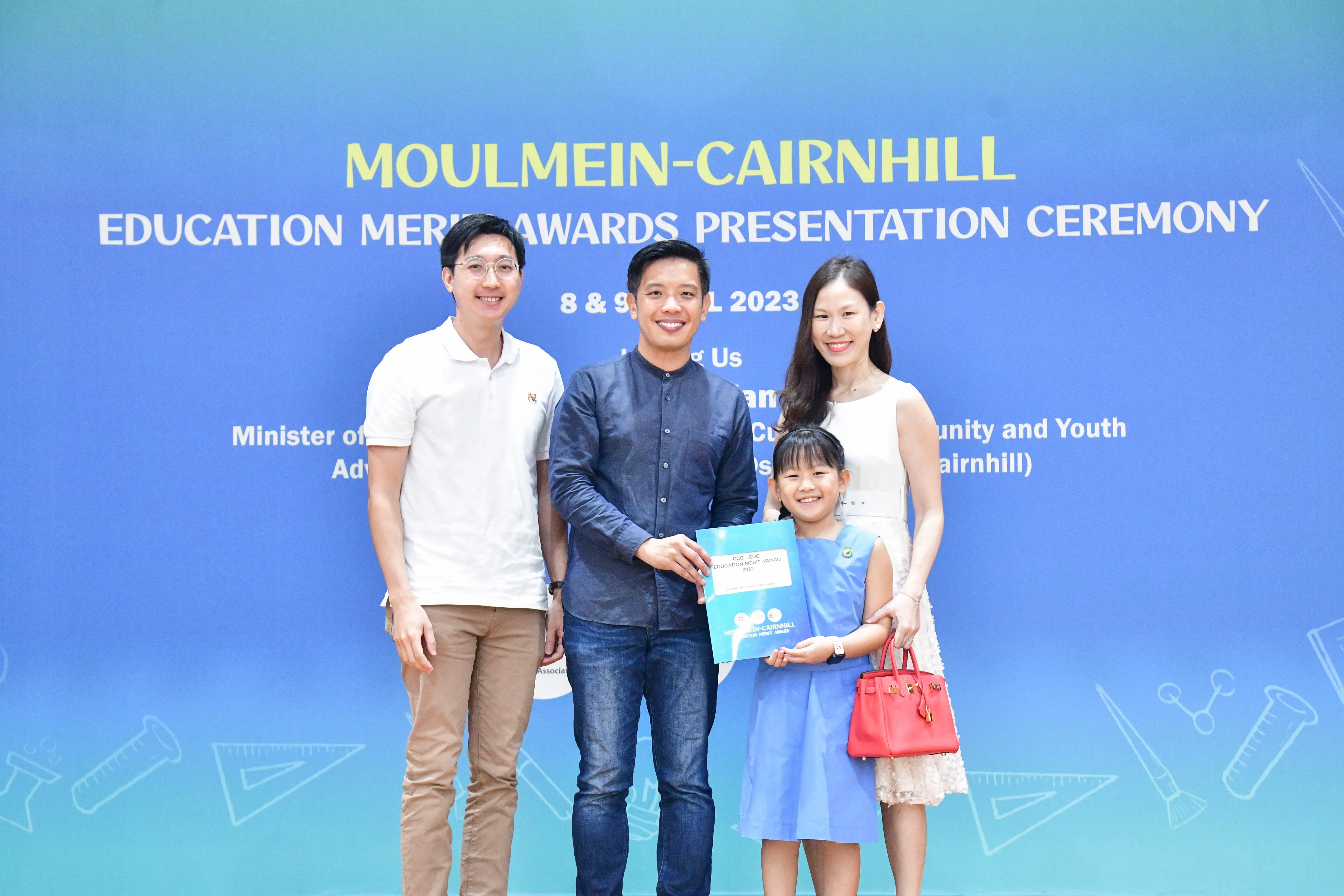 Three adults and a young girl pose with an award certificate at the Moulmein-Cairnhill Education Merit Awards Ceremony 2023.