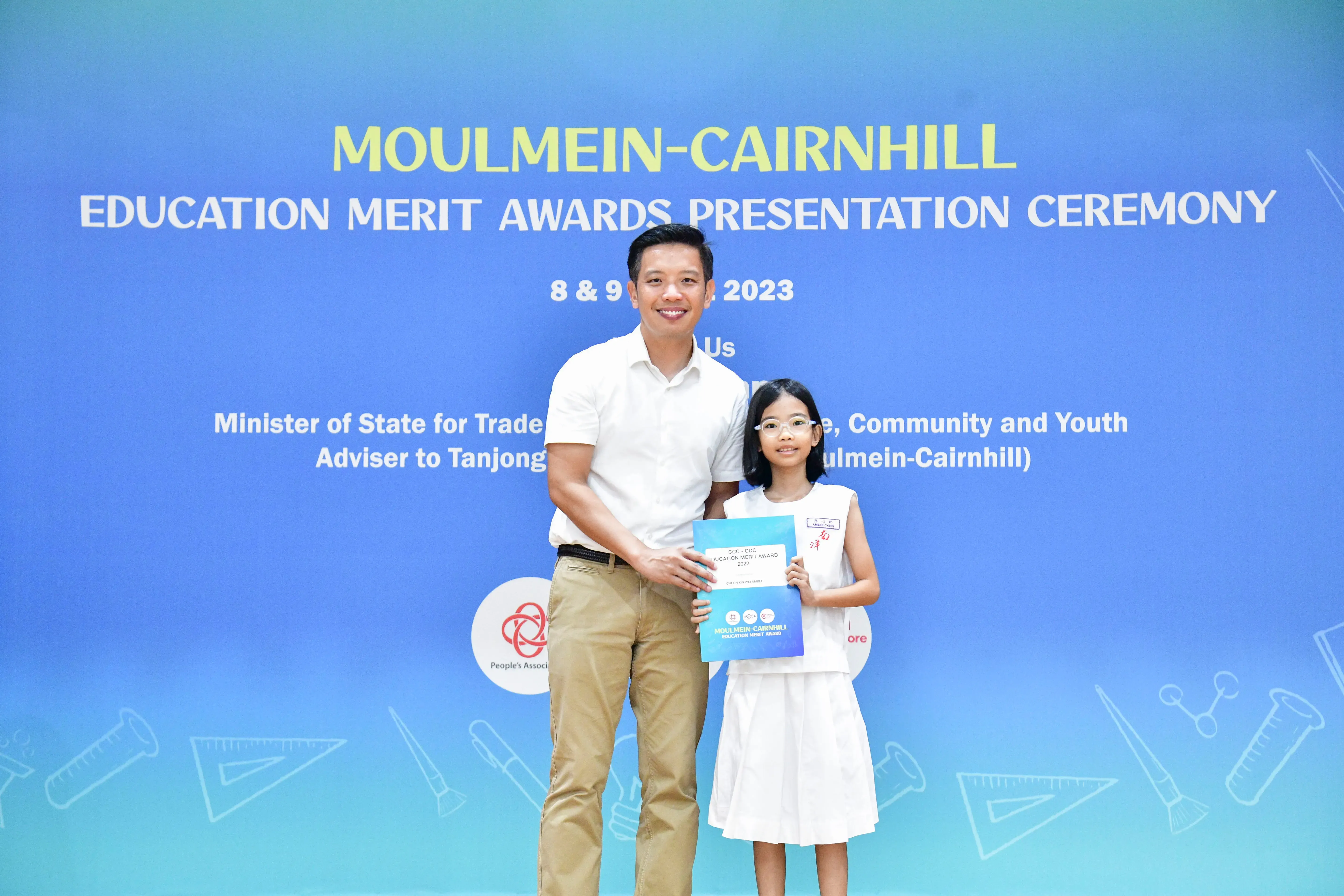 A man and a young girl hold an award certificate at the Moulmein-Cairnhill Education Merit Awards Ceremony 2023.