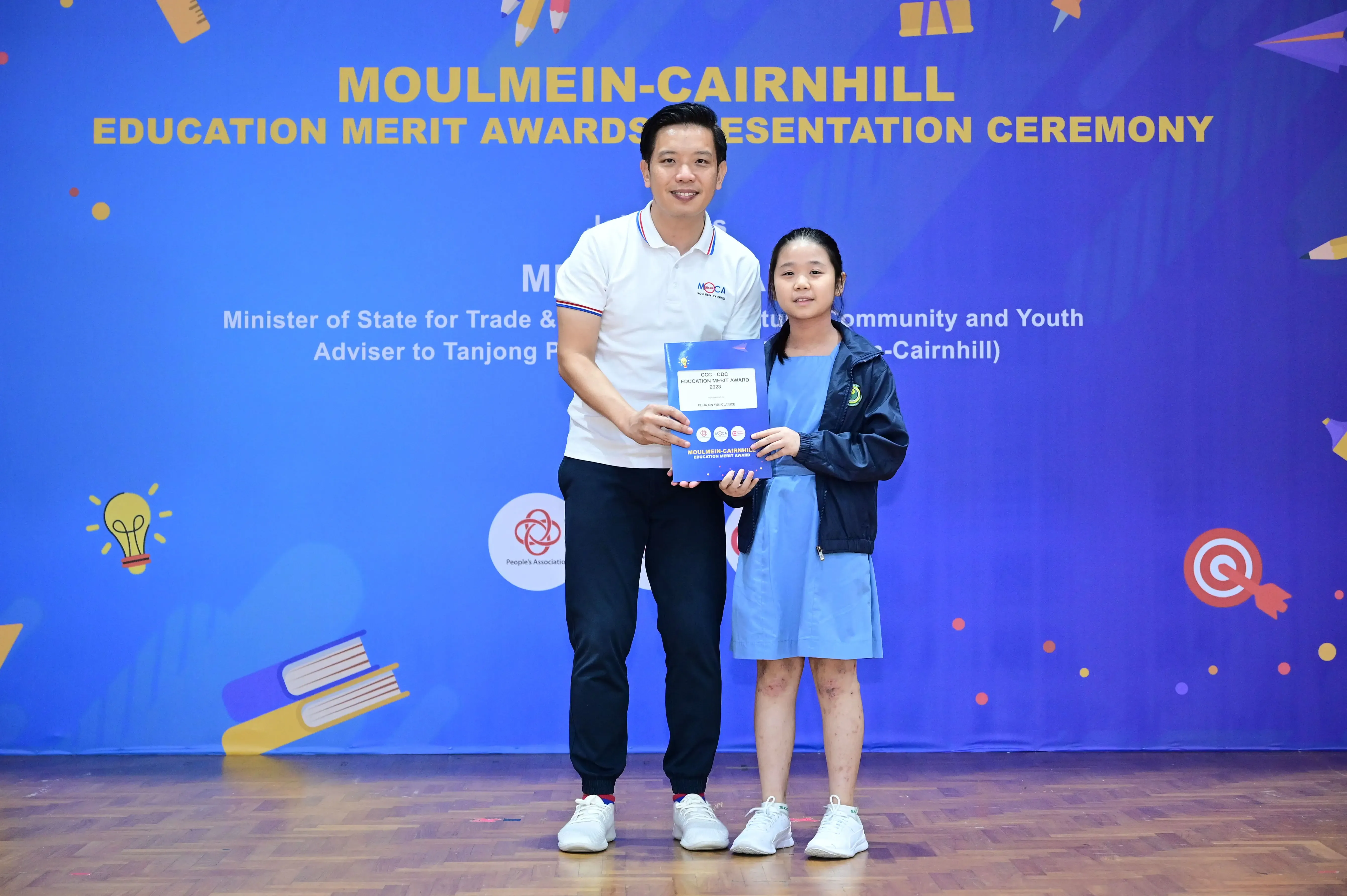 A man and a young girl hold an award certificate at the Moulmein-Cairnhill Education Merit Awards ceremony.