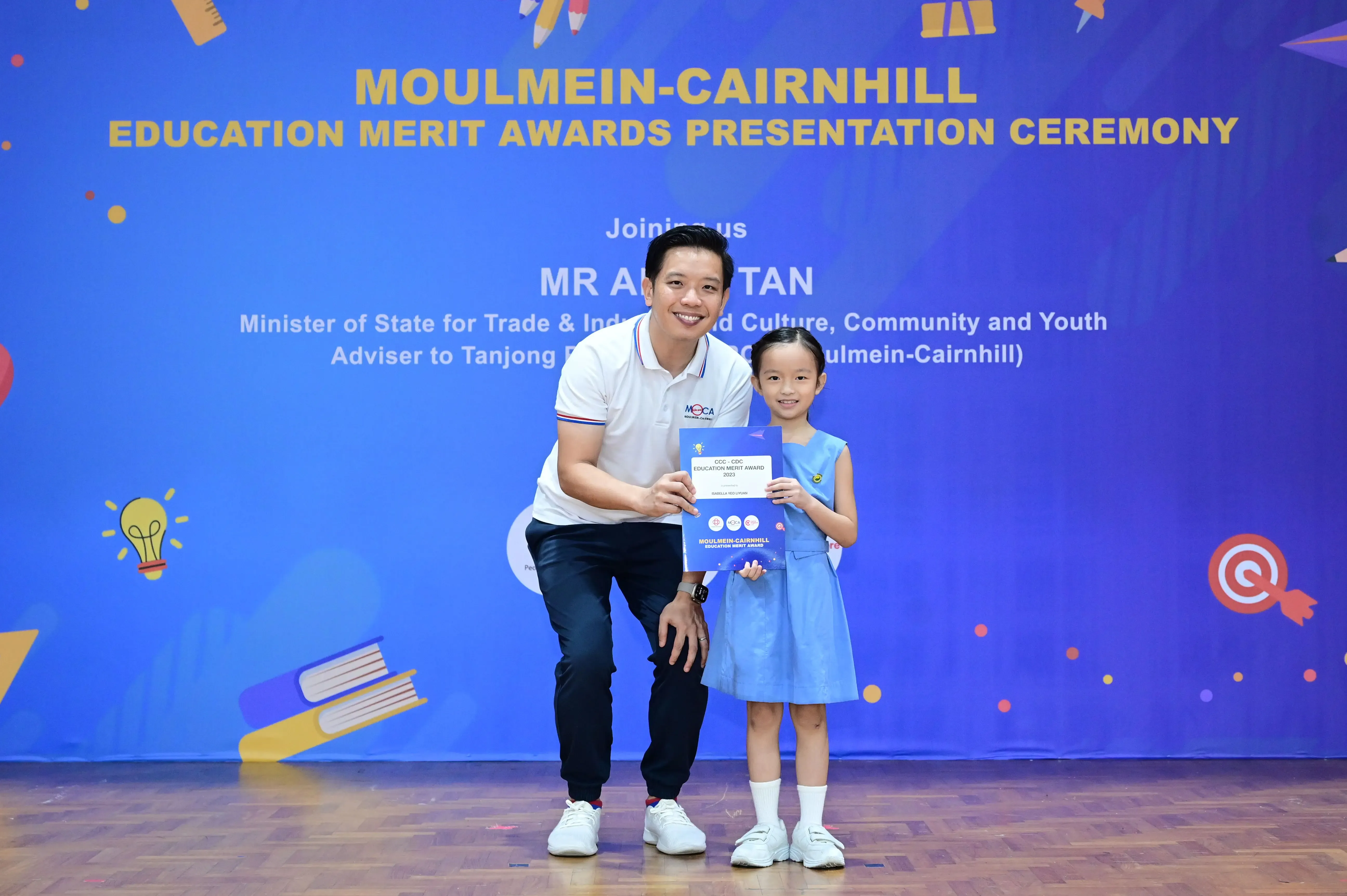 A man and a young girl hold an award certificate at the Moulmein-Cairnhill Education Merit Awards ceremony.