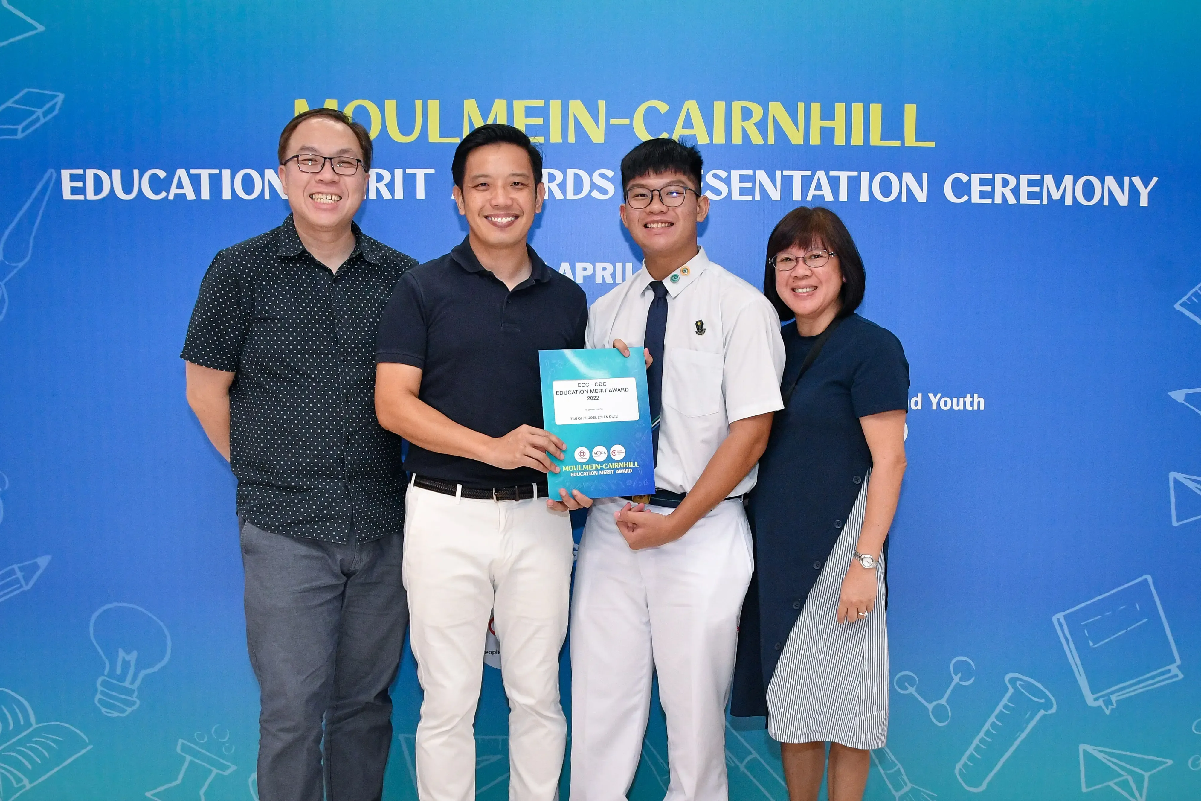 Four people smile while holding a certificate at the Moulmein-Cairnhill Education Merit Awards Presentation Ceremony.