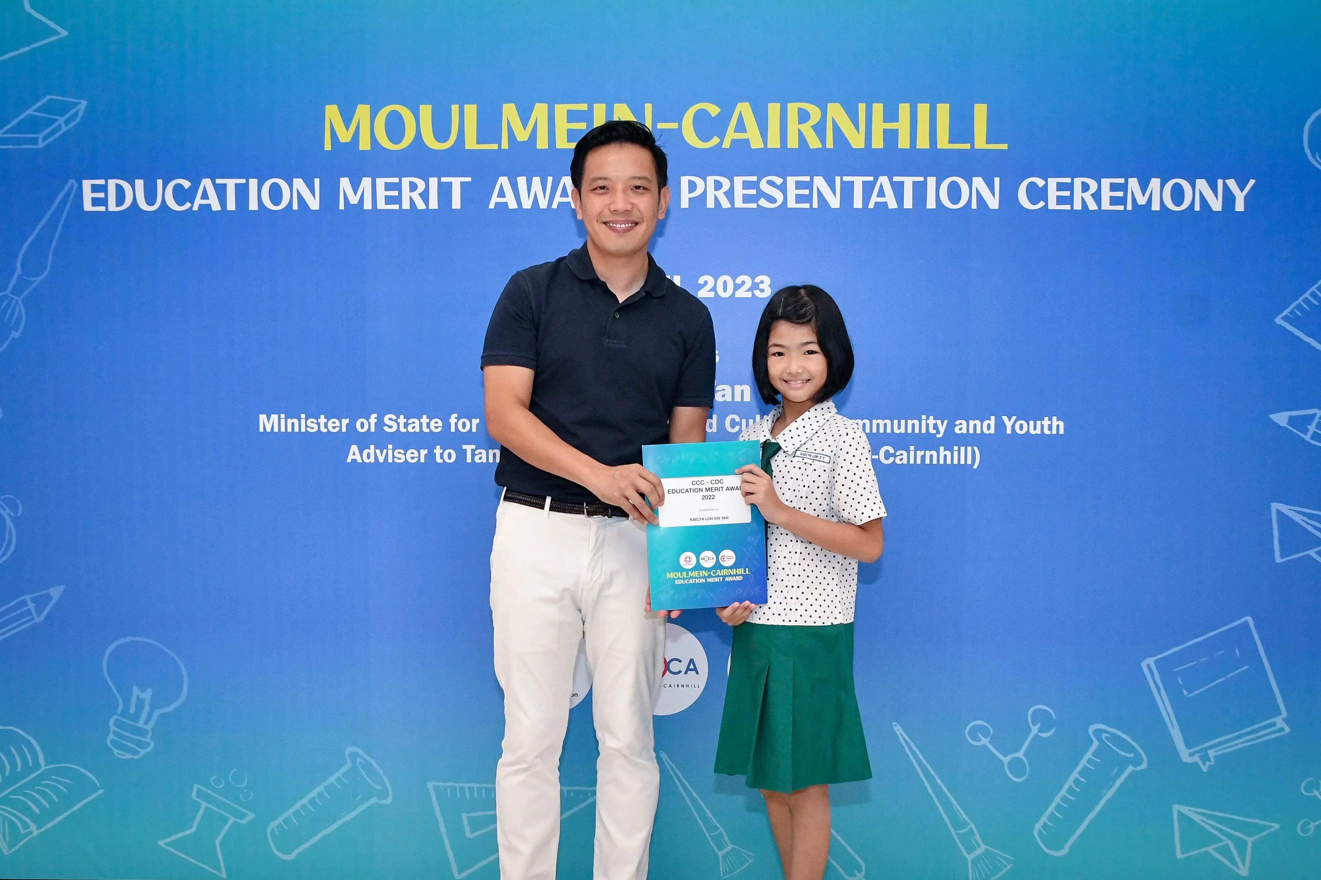 A man and a young girl hold an award certificate at the 2023 Moulmein-Cairnhill Education Merit Award Presentation Ceremony.