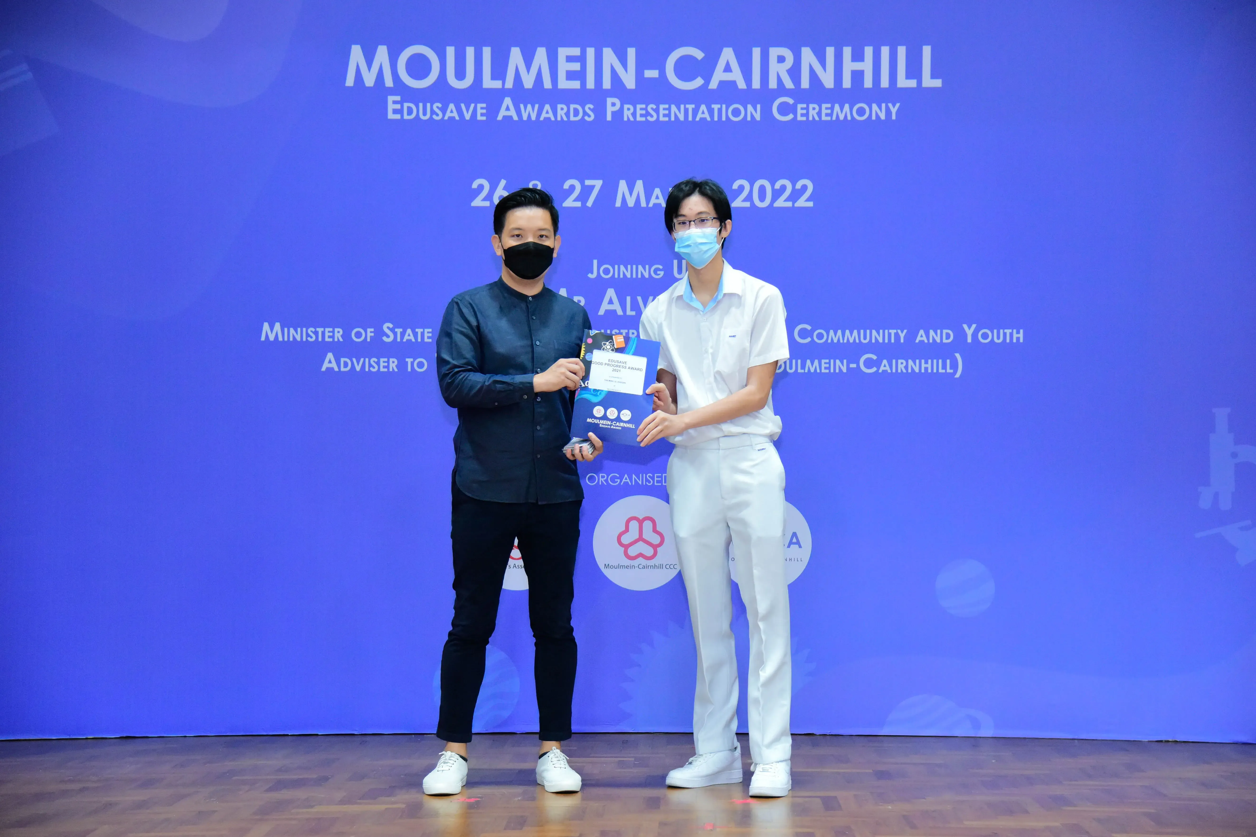 Two masked individuals holding an award certificate at the Moulmein-Cairnhill Edusave Awards Ceremony in May 2022.