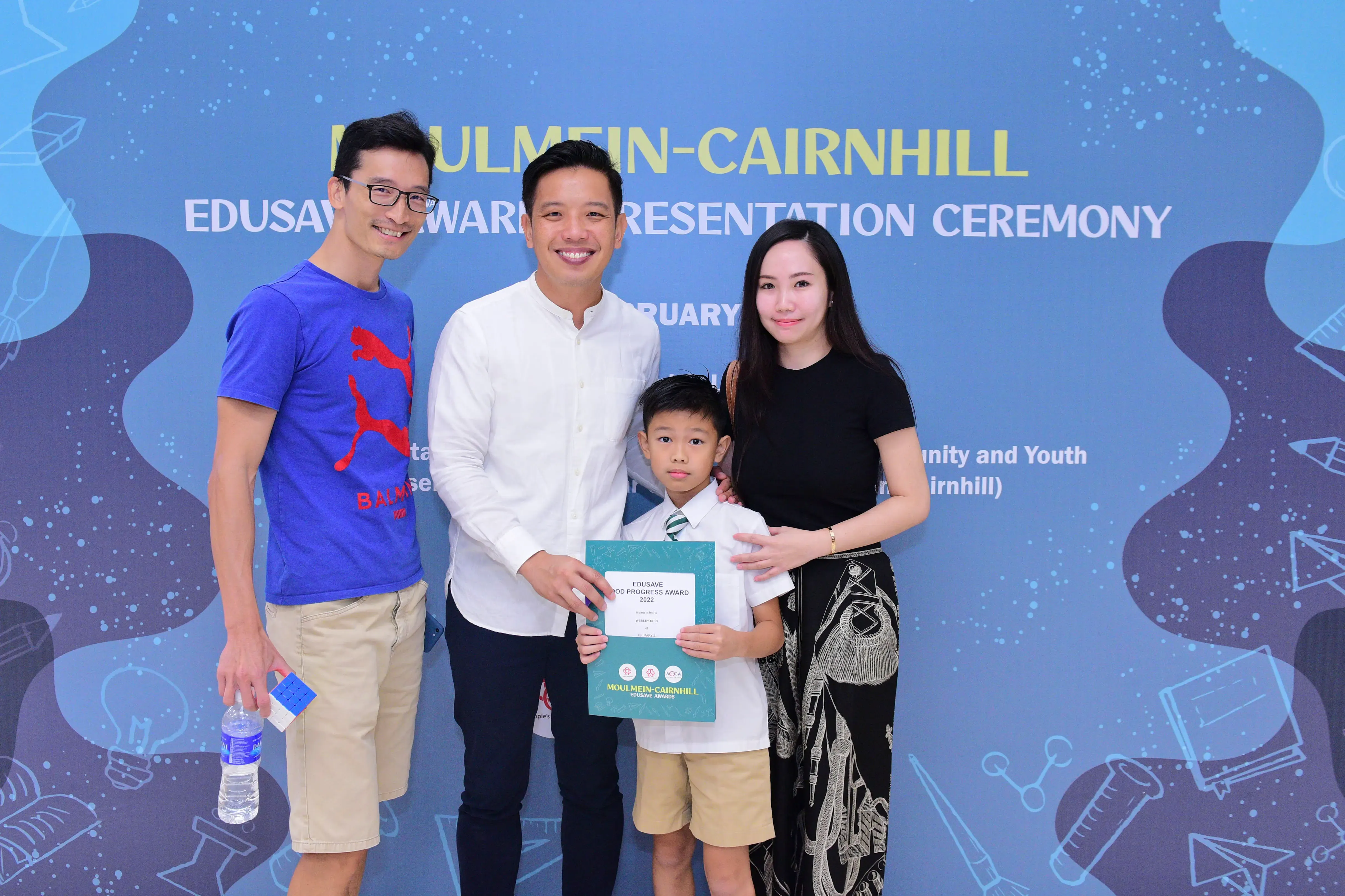 Three adults and a boy holding an Edusave award certificate at the Moulmein-Cairnhill Award Presentation Ceremony.