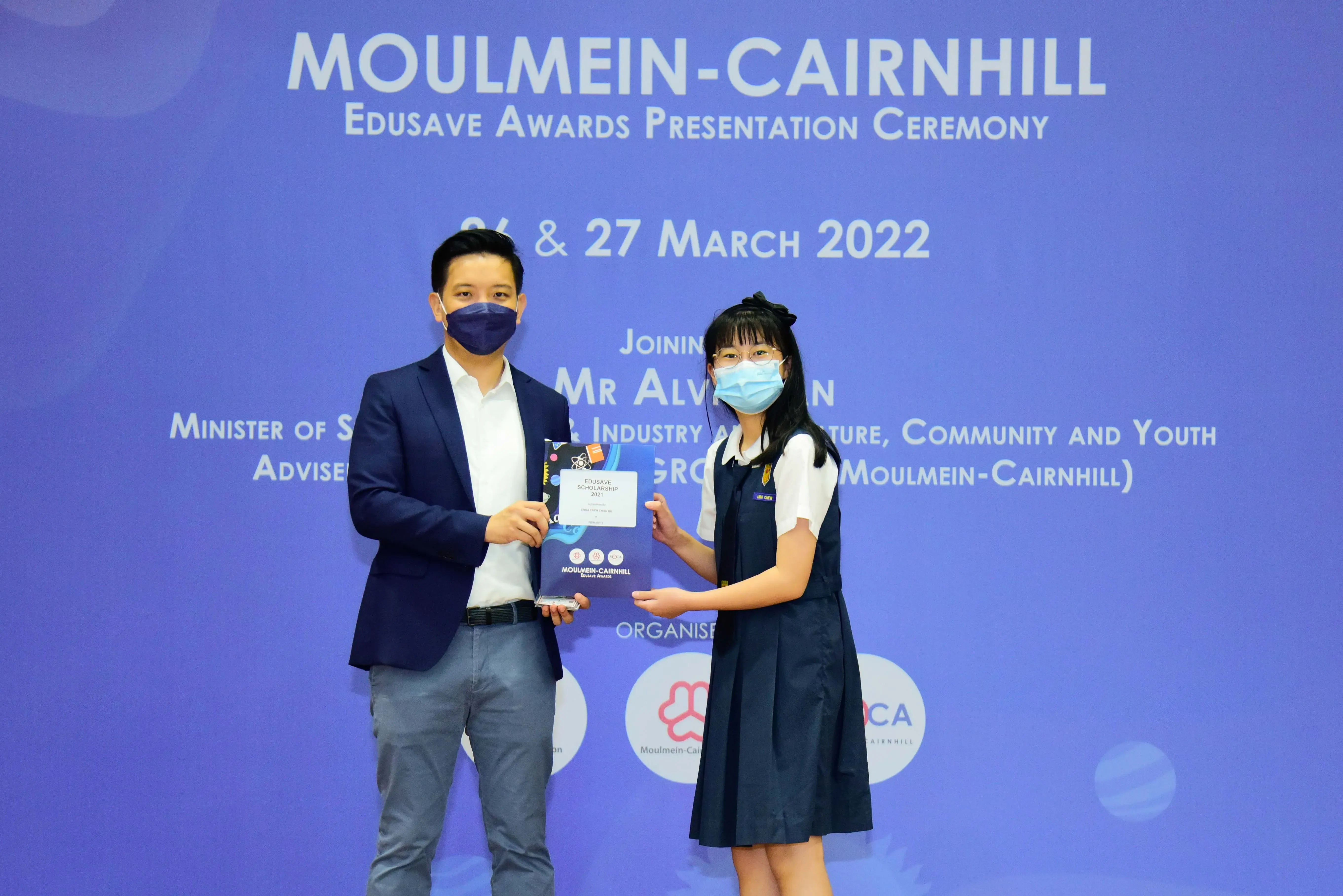 A man and a young girl in masks hold an award at the Moulmein-Cairnhill Edusave Awards Ceremony, March 2022.