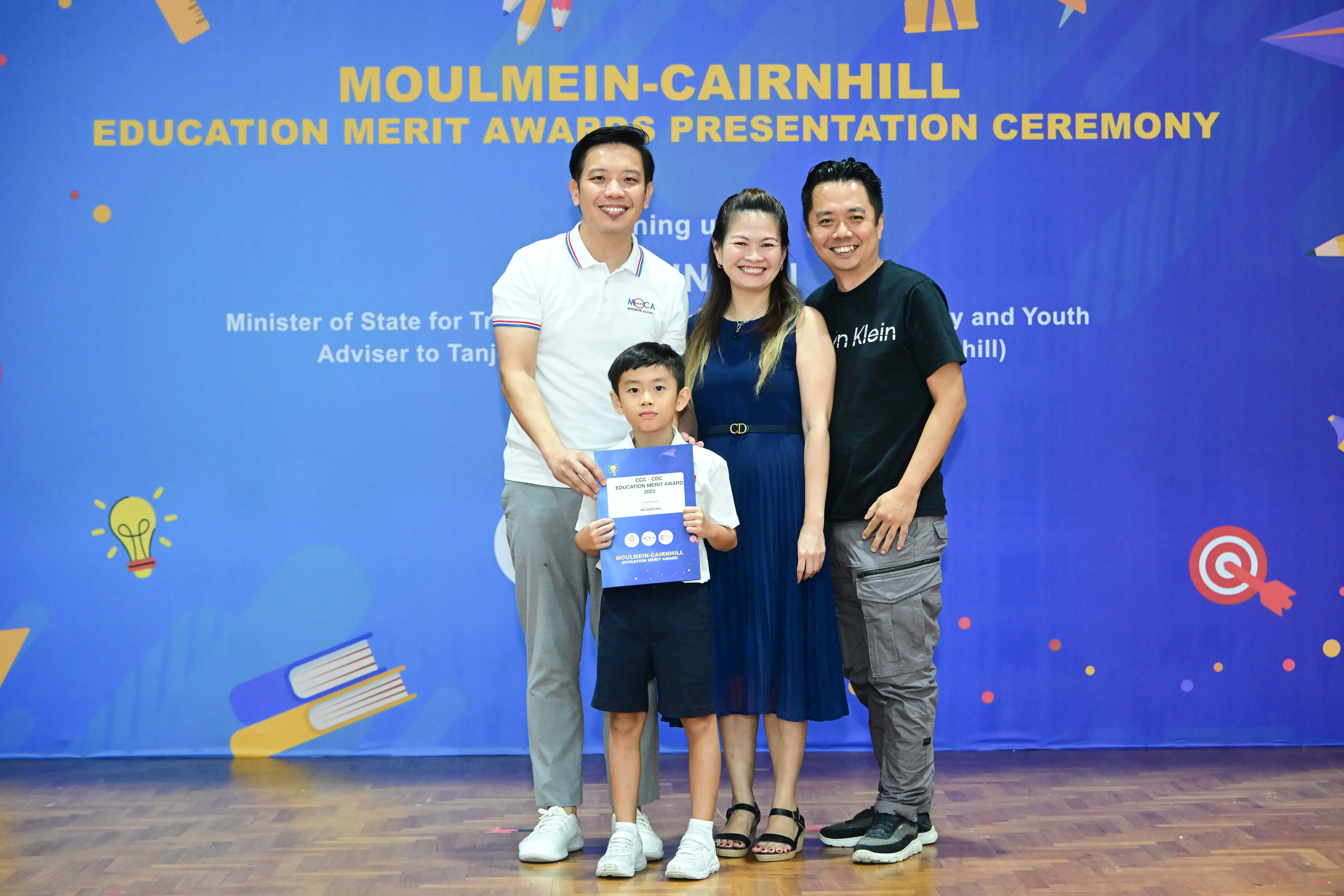 Three adults and a young boy holding an award certificate pose at the Moulmein-Cairnhill Education Merit Awards ceremony.