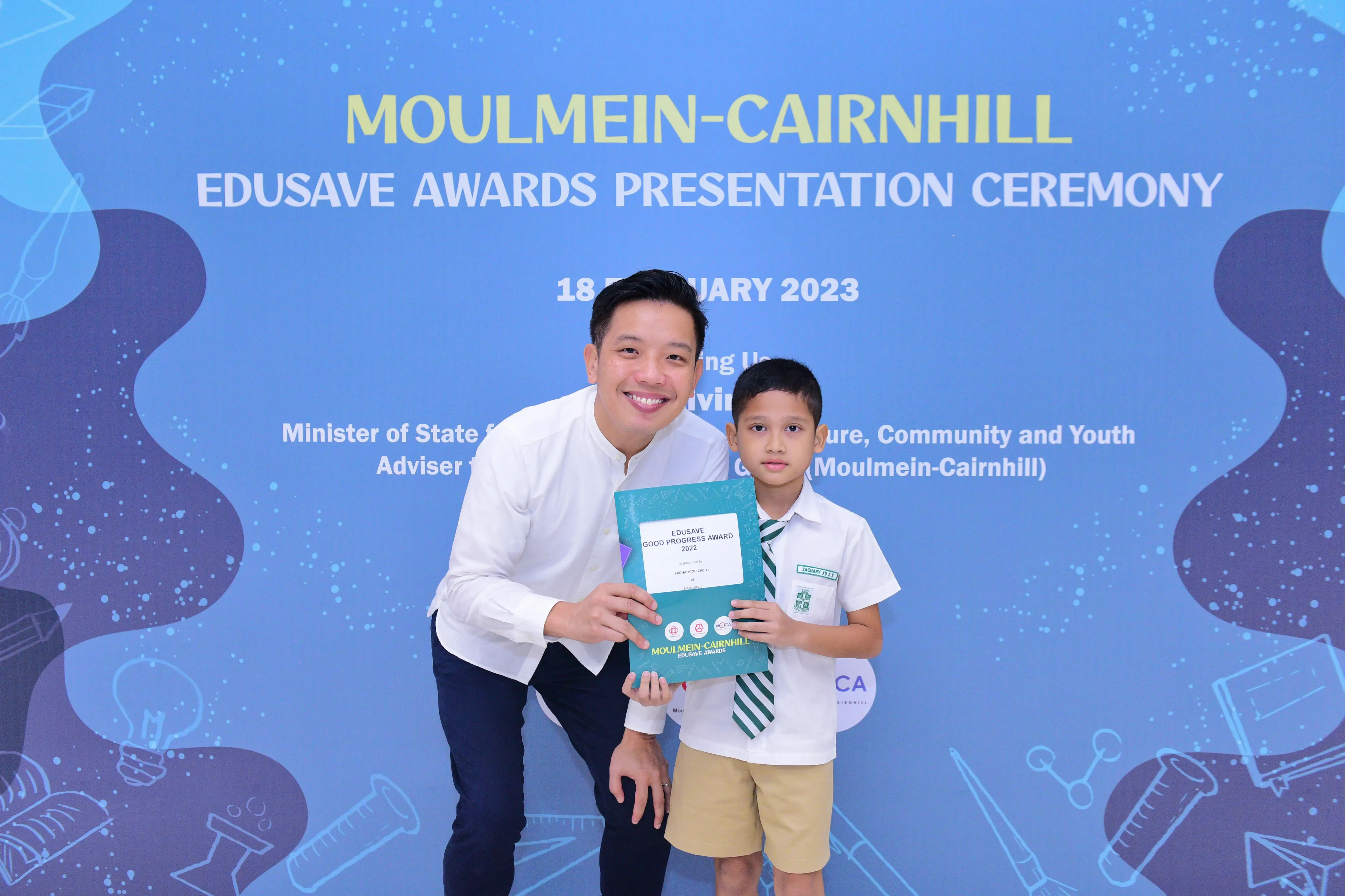 A man and a young boy hold an Edusave Good Progress Award certificate at the Moulmein-Cairnhill Awards Ceremony 2023.