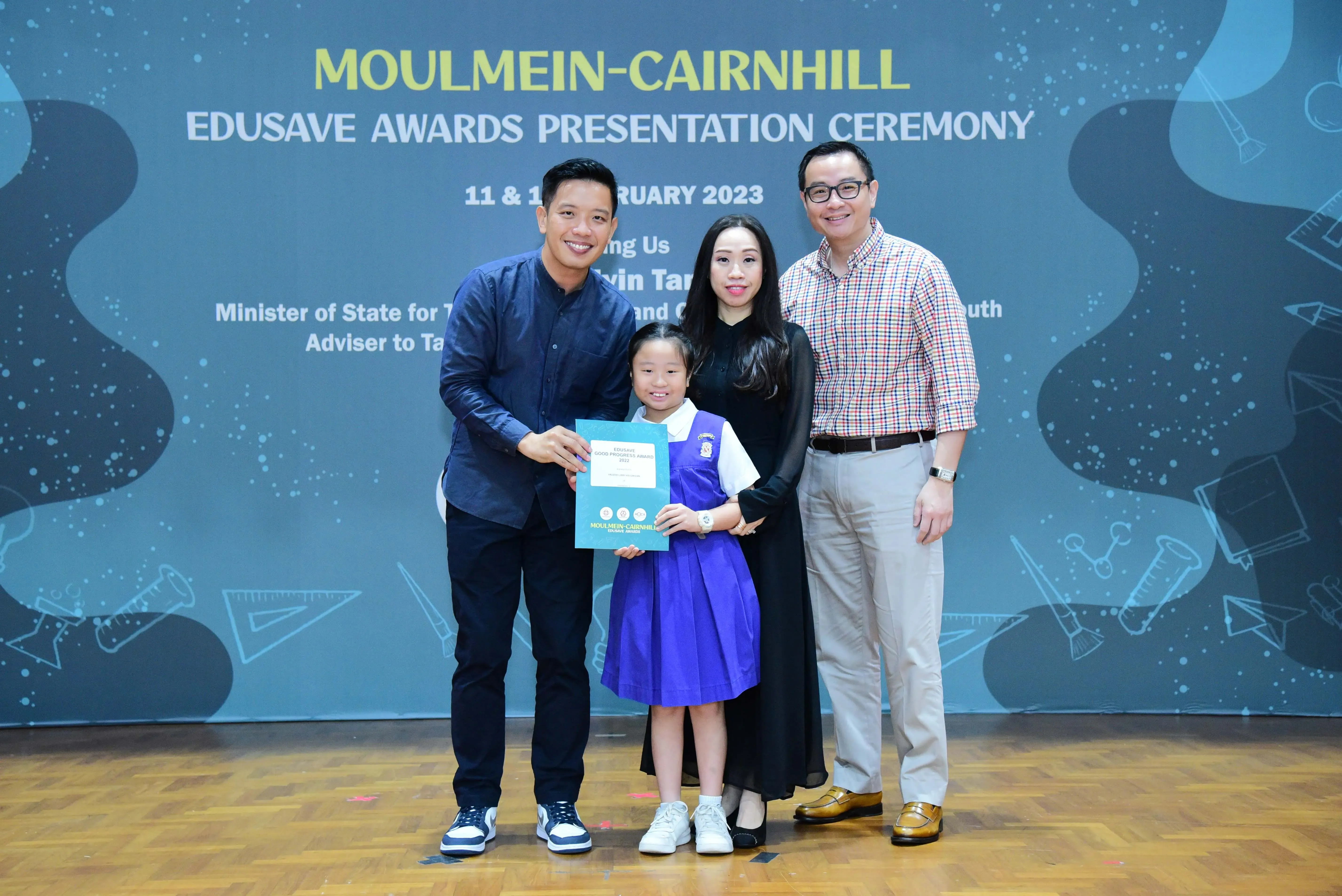 Three adults and a young girl in school uniform hold a certificate at Moulmein-Cairnhill Edusave Awards Ceremony 2023.