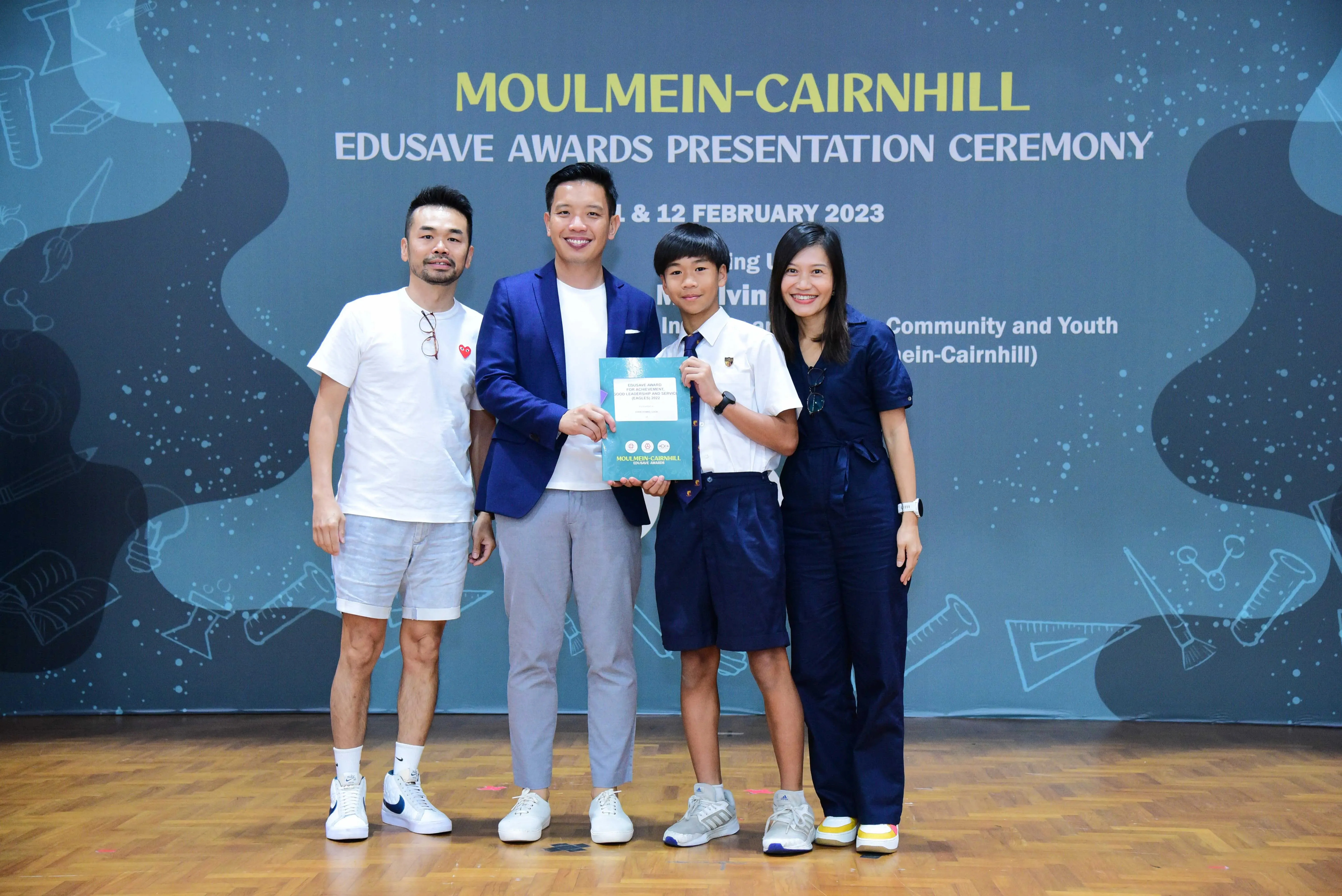 Four people pose at the Moulmein-Cairnhill Edusave Awards Presentation Ceremony, with a student holding a certificate.