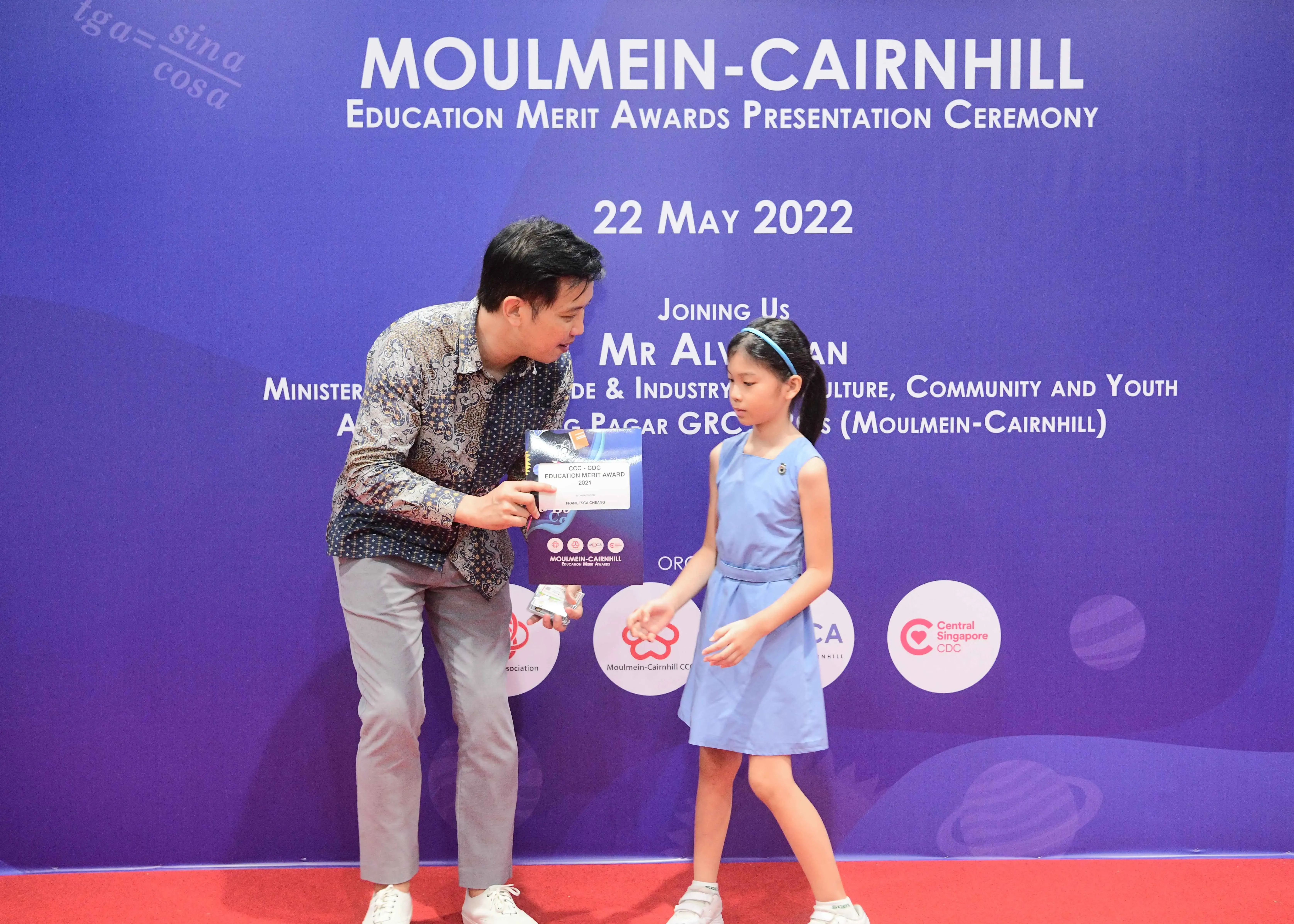A man hands an award certificate to a young girl at the Moulmein-Cairnhill Education Merit Awards on 22 May 2022.