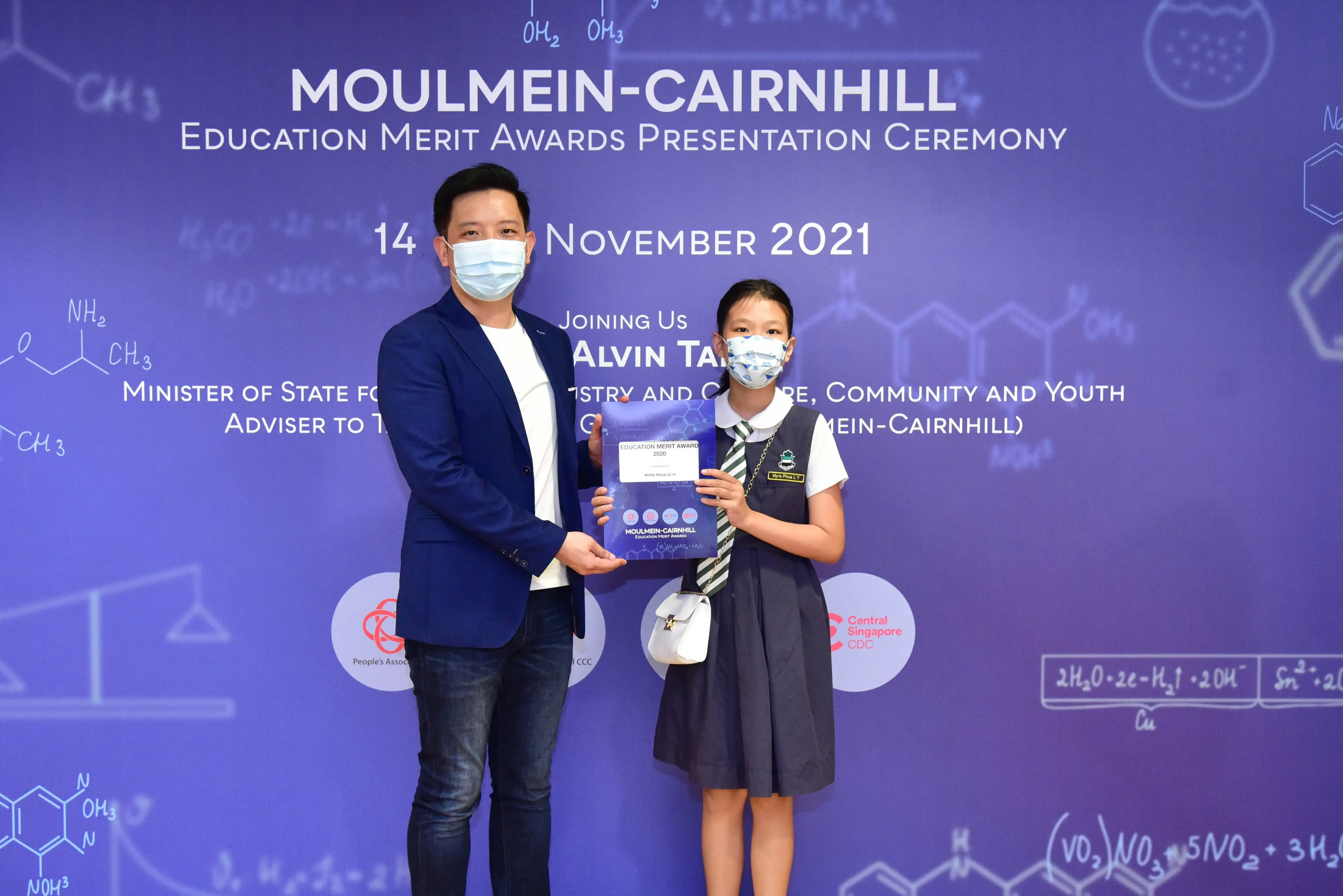 A man and a young girl in school uniform hold a certificate at the Moulmein-Cairnhill Education Merit Awards 2021.