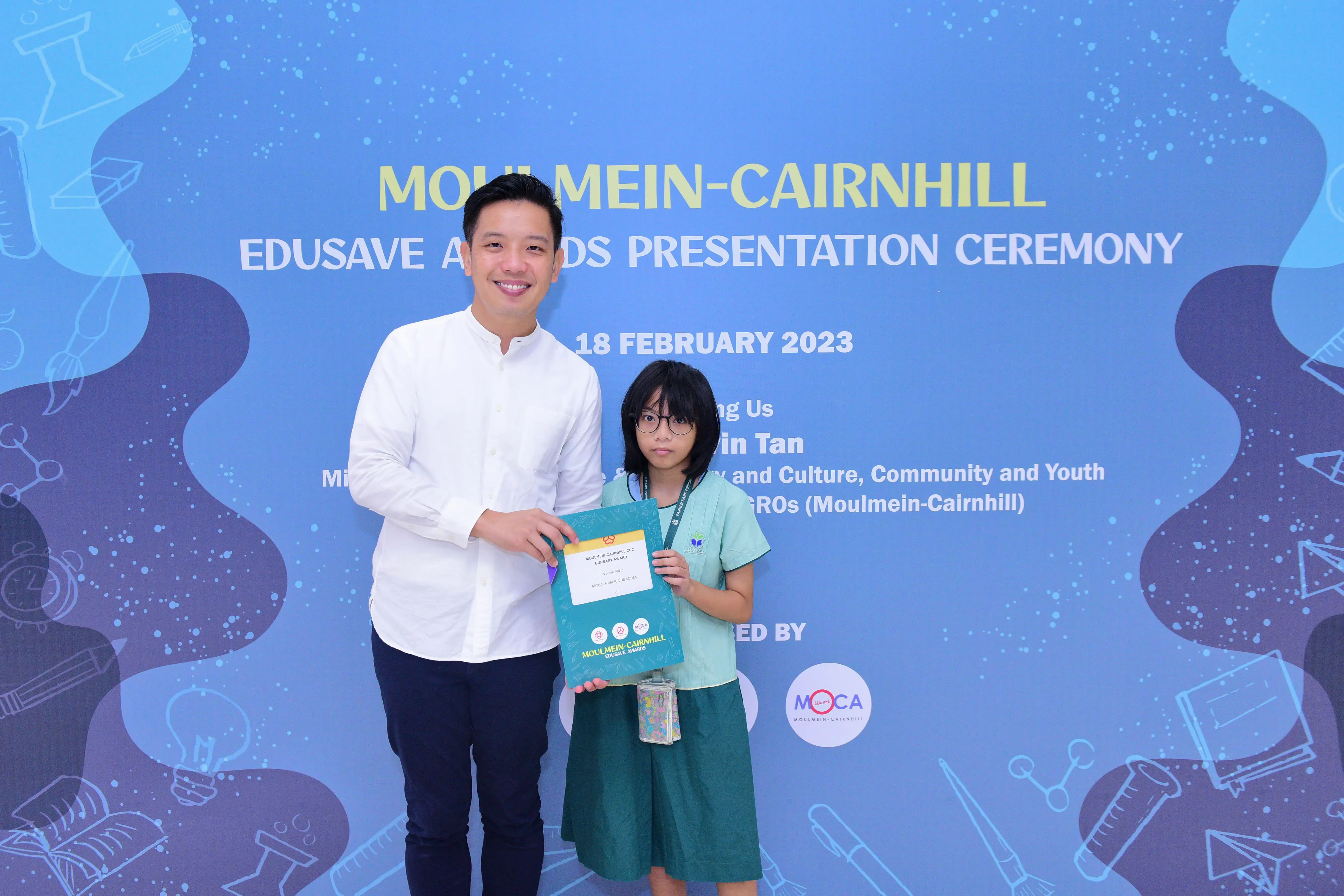 A man and a young girl hold an award folder at the Moulmein-Cairnhill Edusave Awards Ceremony on 18 February 2023.