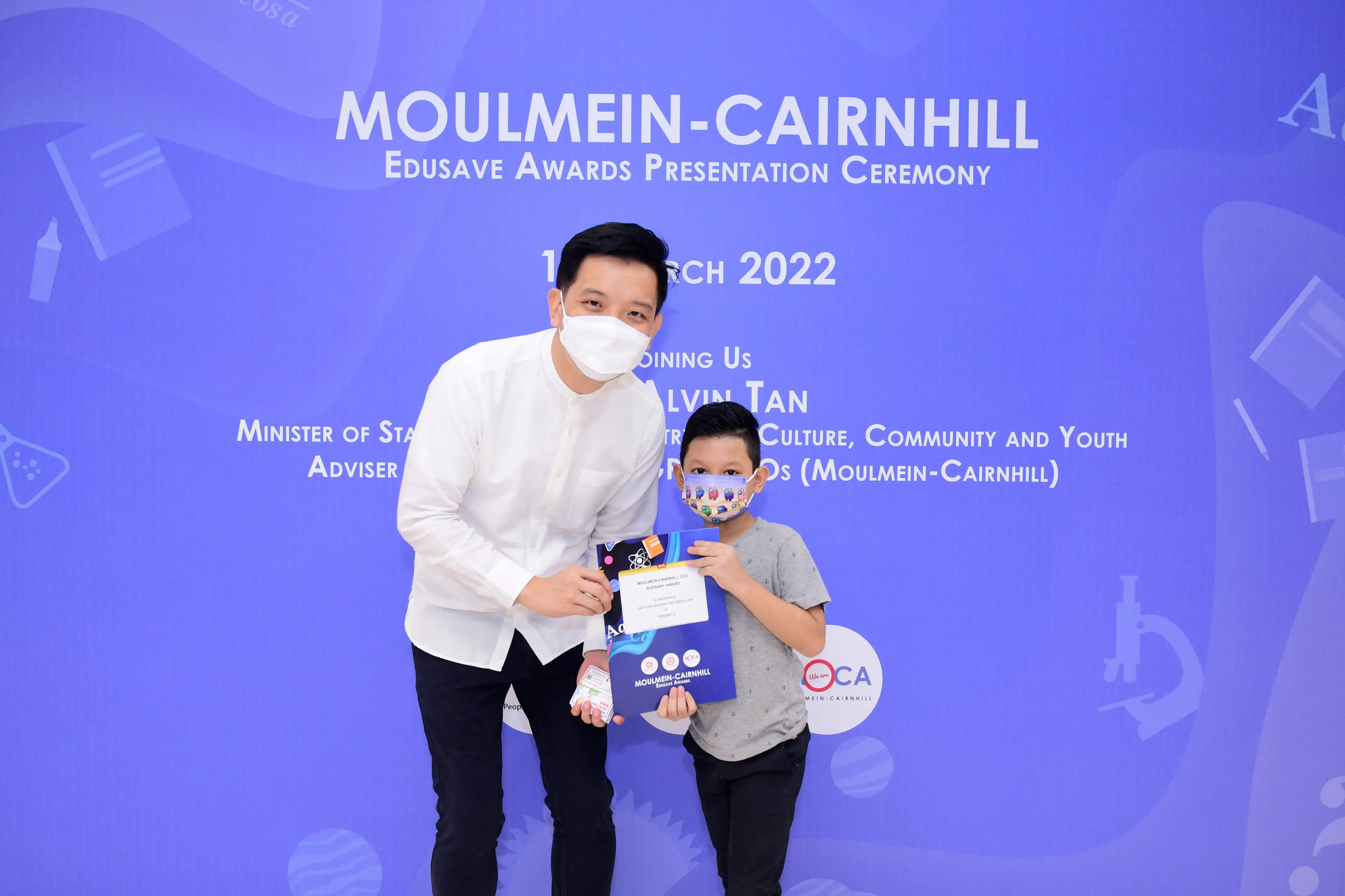 An adult and a young boy wearing masks pose with an award at the Moulmein-Cairnhill Edusave Awards Ceremony 2022.